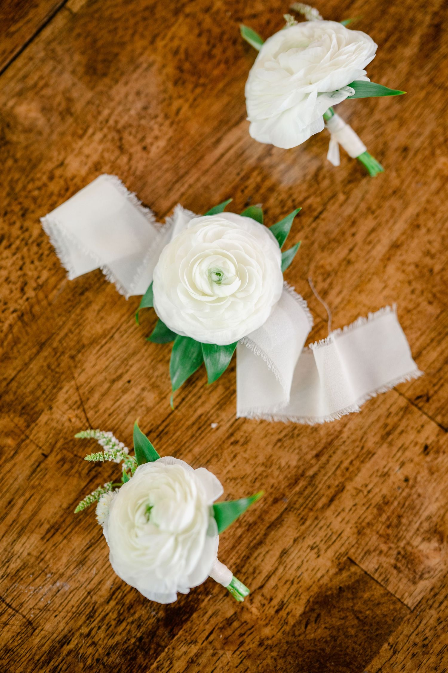 White ranunculus flowers scattered on a rustic wooden surface creating a romantic composition.