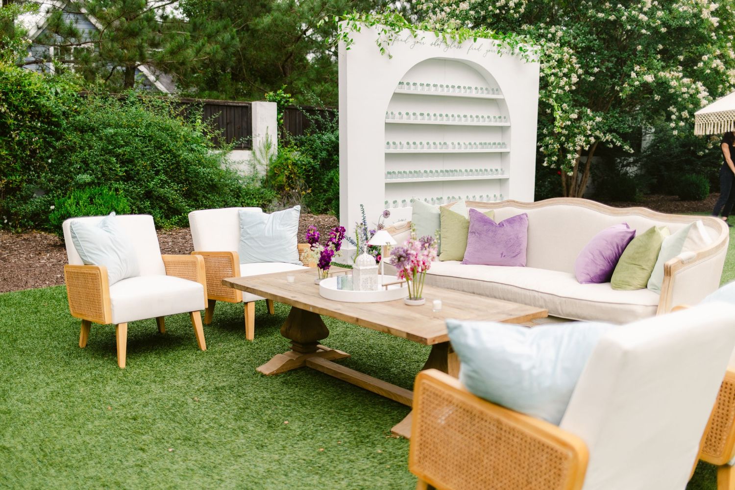 Modern outdoor patio furniture with white cushions arranged on a green lawn near lush landscaping.
