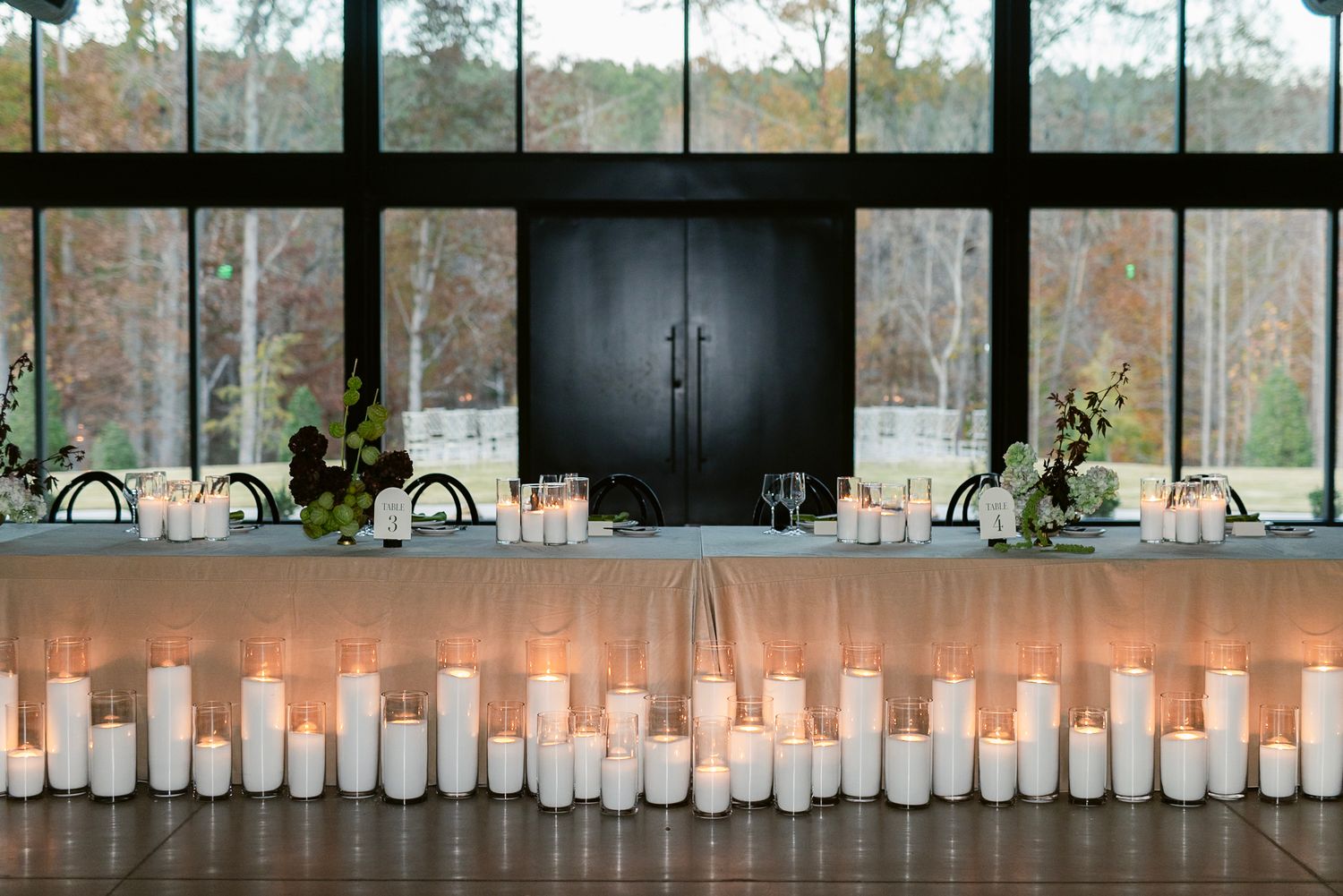 White pillar candles line a rustic wooden shelf creating an elegant ambiance at a wedding reception venue.