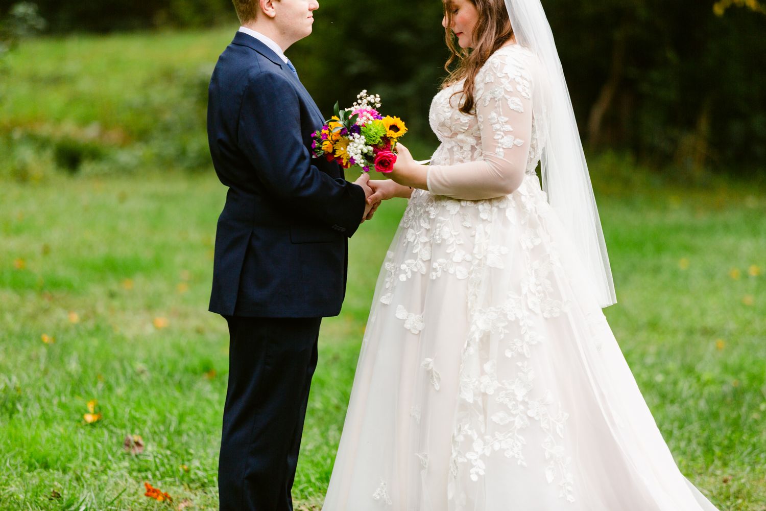A bride and groom exchange vows in a garden setting with the bride wearing a lace dress and holding flowers.