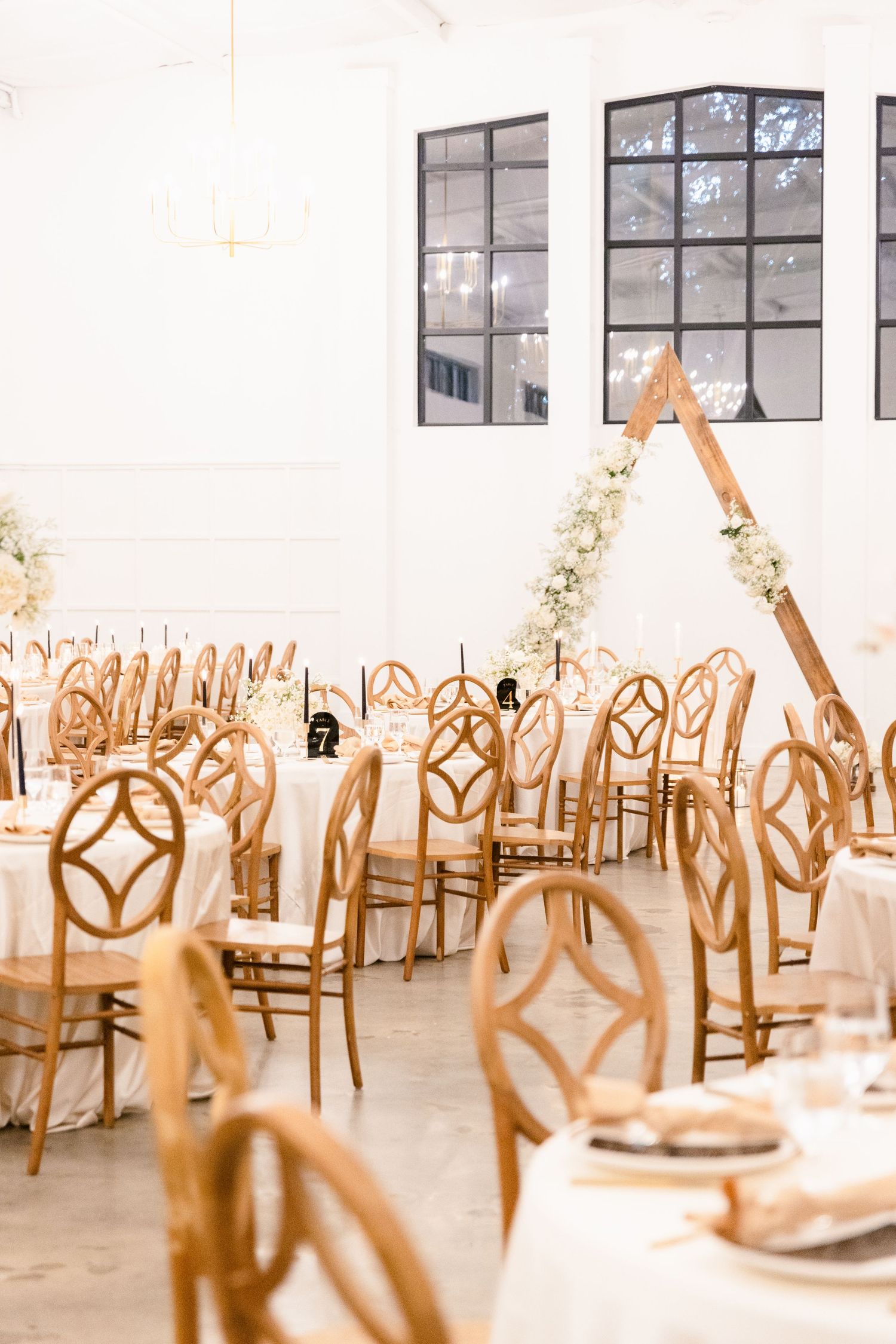 Wedding reception setup with wooden chairs and geometric designs in a bright white venue.