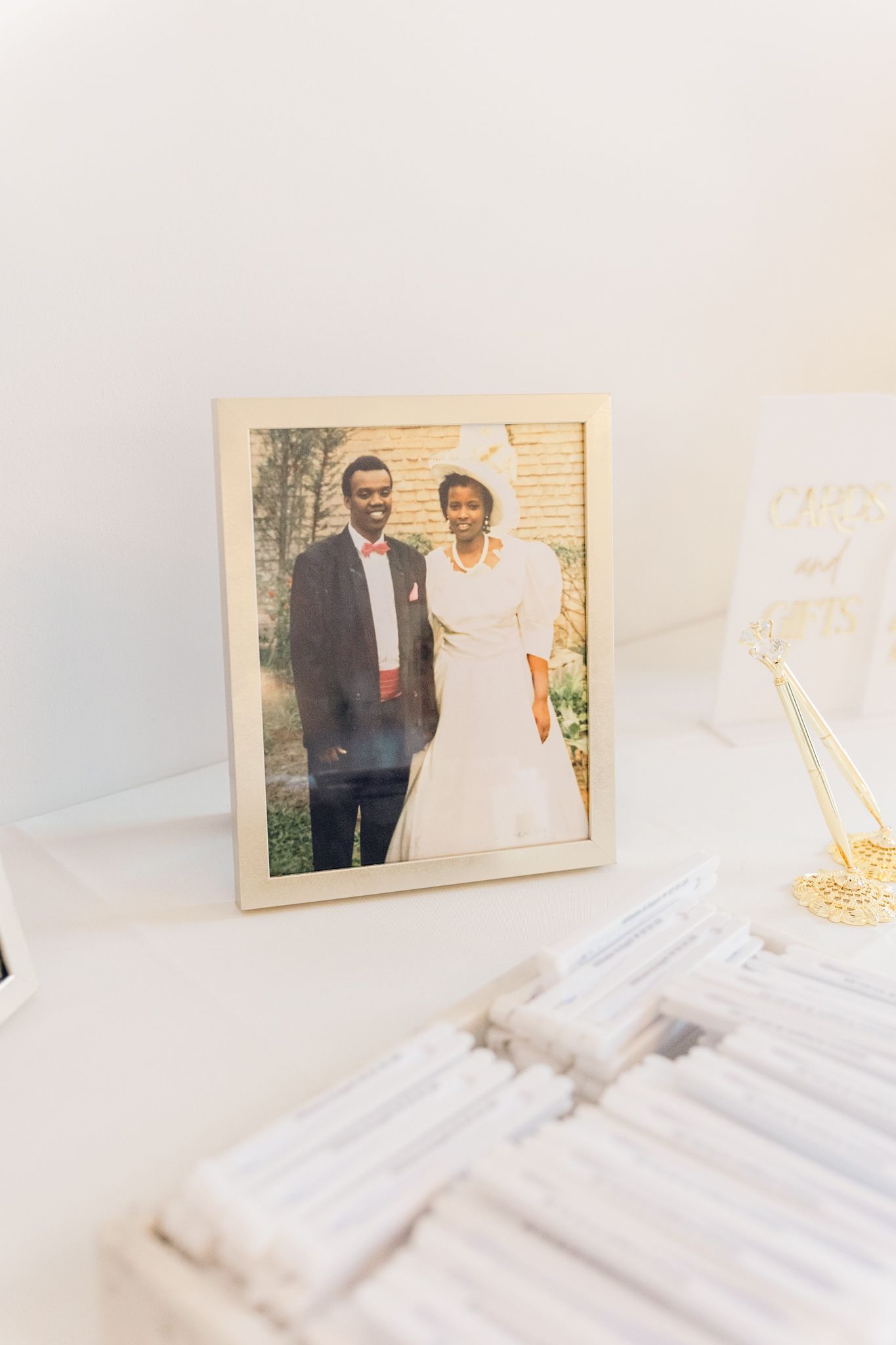 A framed wedding photo sits on a white surface next to other photo frames in a bright, minimalist setting.