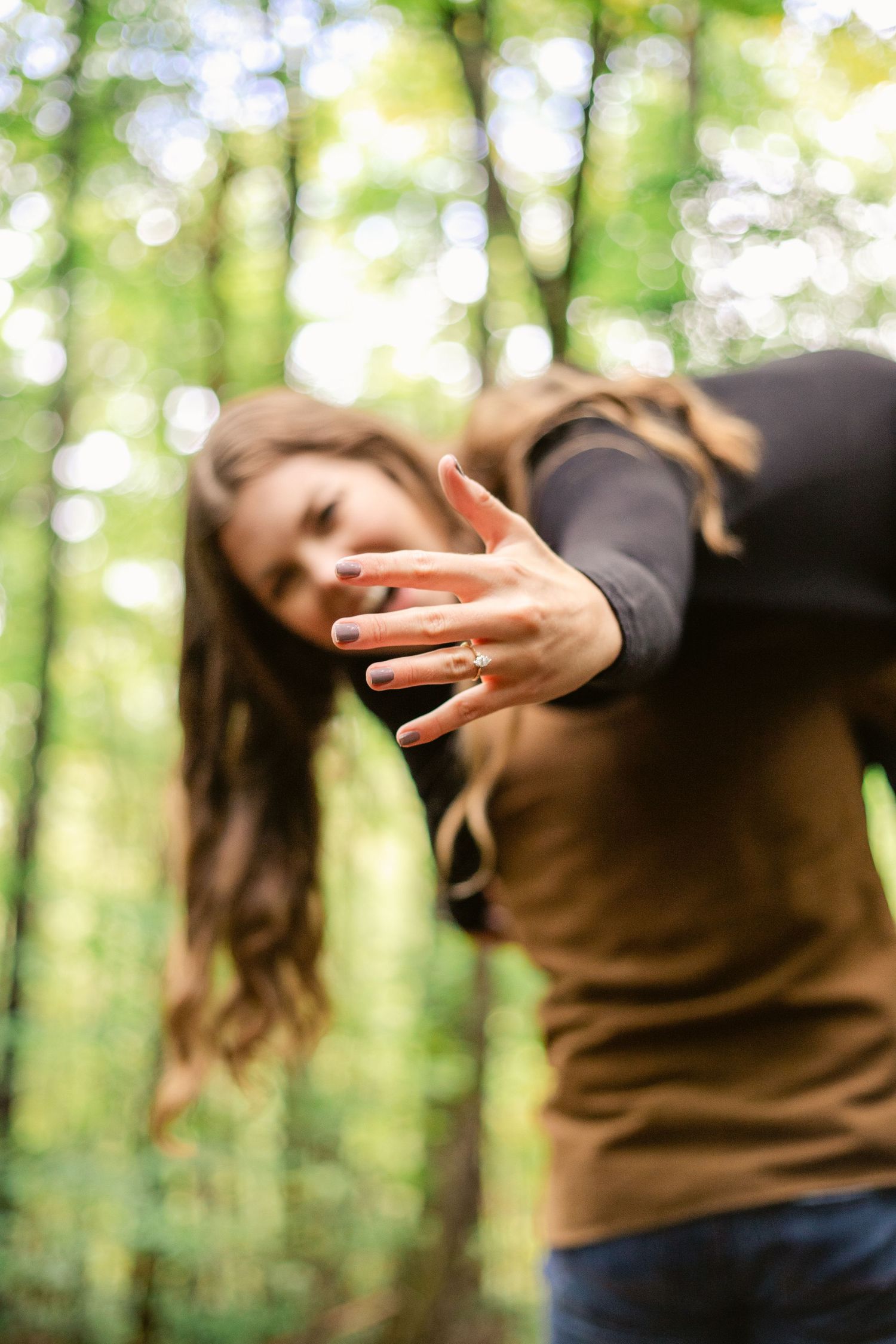 Person reaching out their hand in a dynamic pose with sunlit forest bokeh in the background.