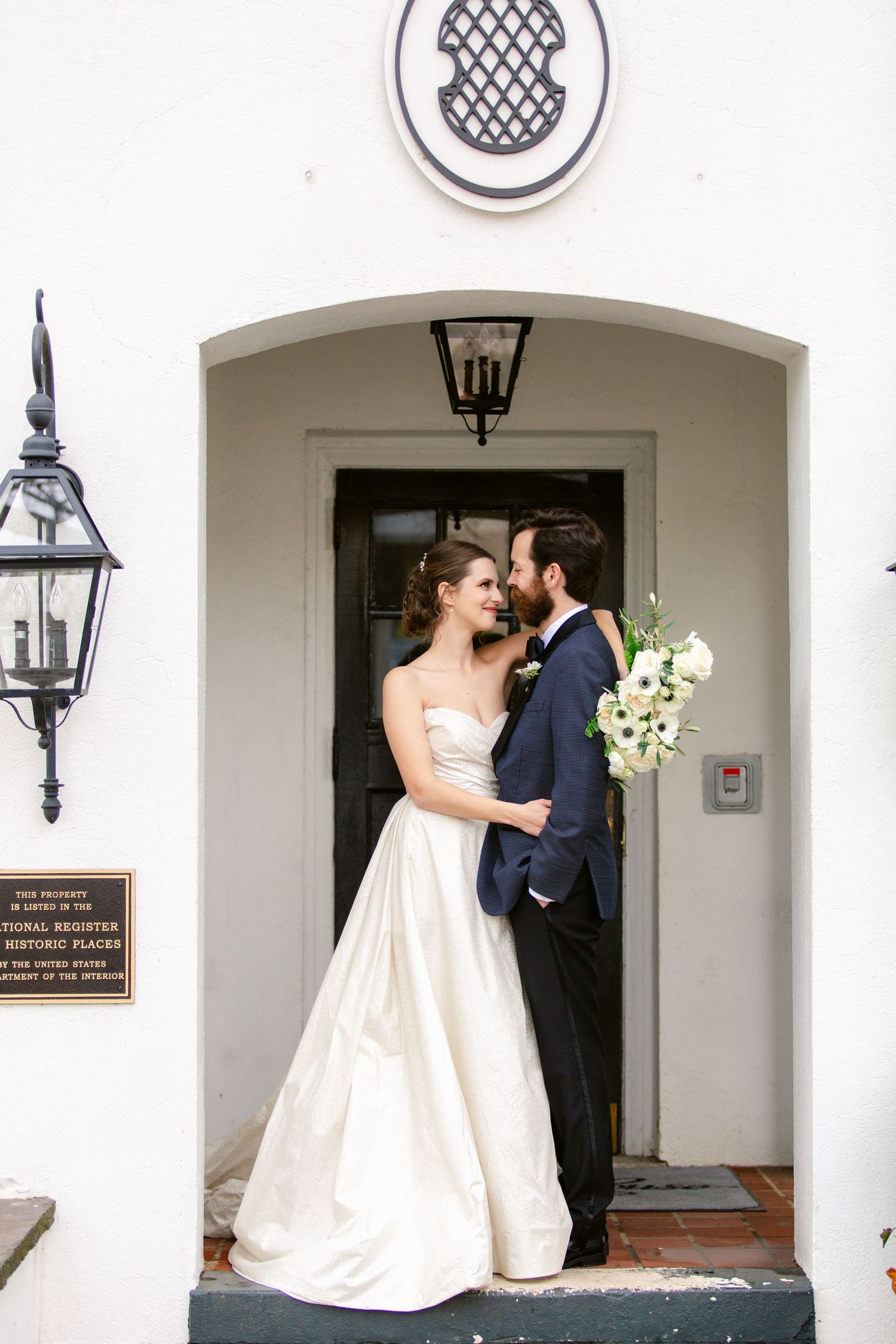 Wedding couple shares an intimate moment under an elegant white archway entrance.