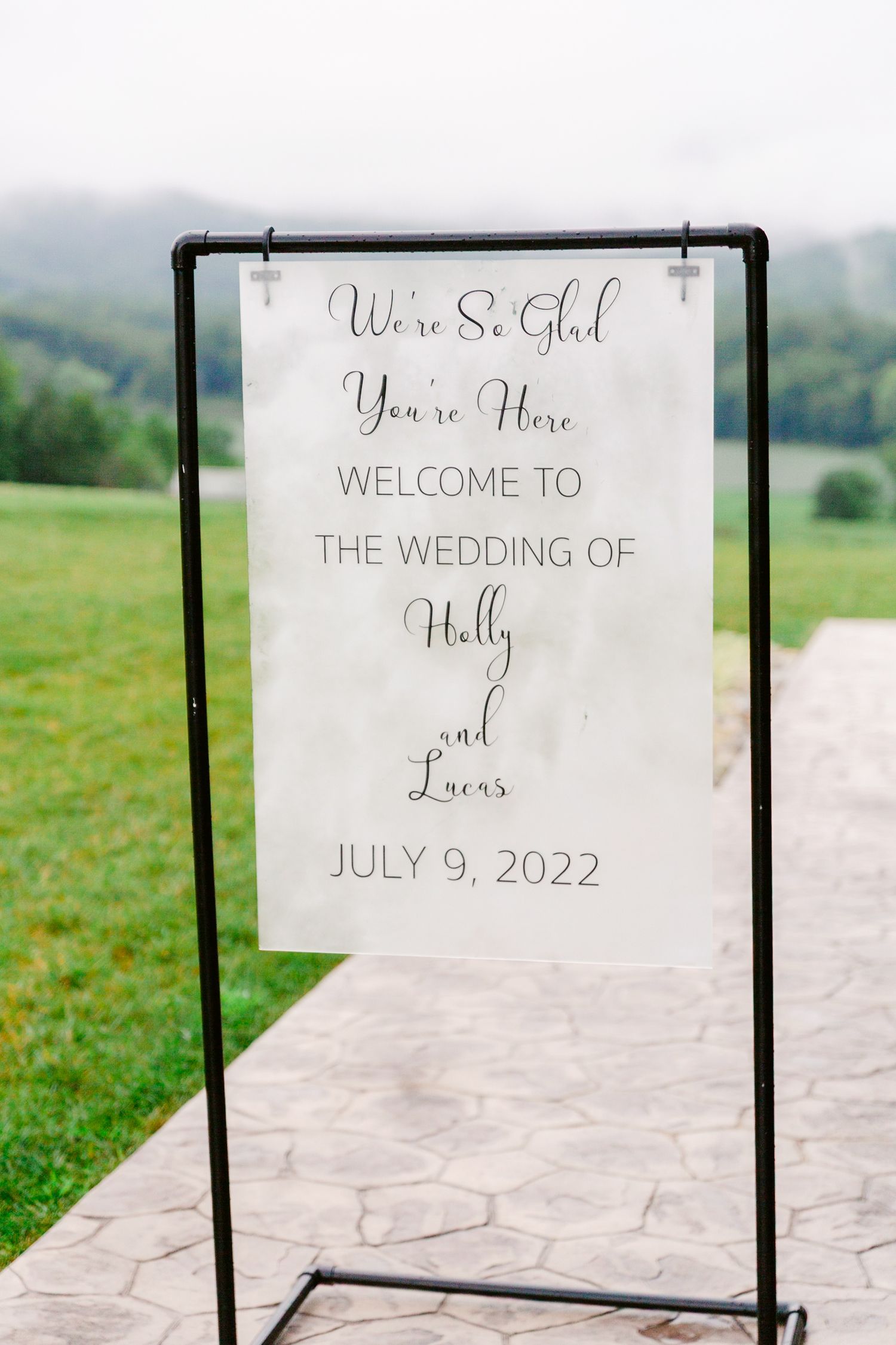 Wedding welcome sign displayed on black metal stands against a misty mountain backdrop.
