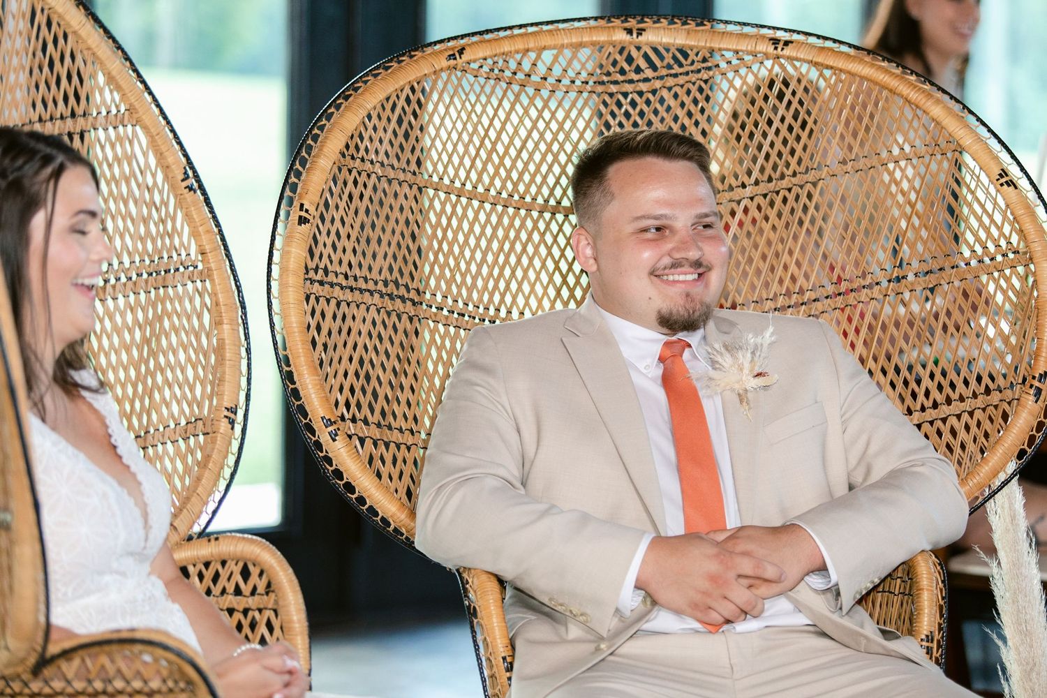 Wedding party seated in a row of vintage peacock chairs at an outdoor celebration.