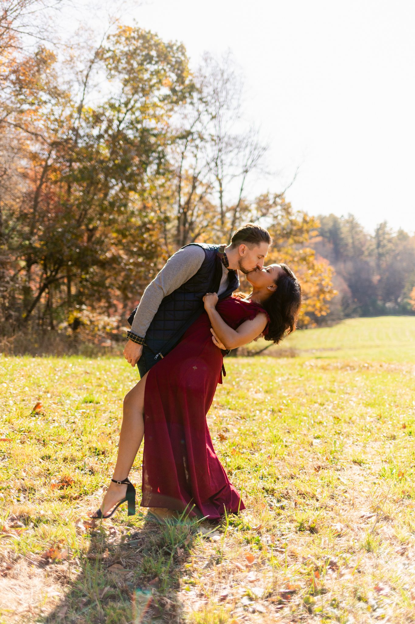 A romantic couple embraces in a fall meadow with autumn foliage and golden sunlight in the background.