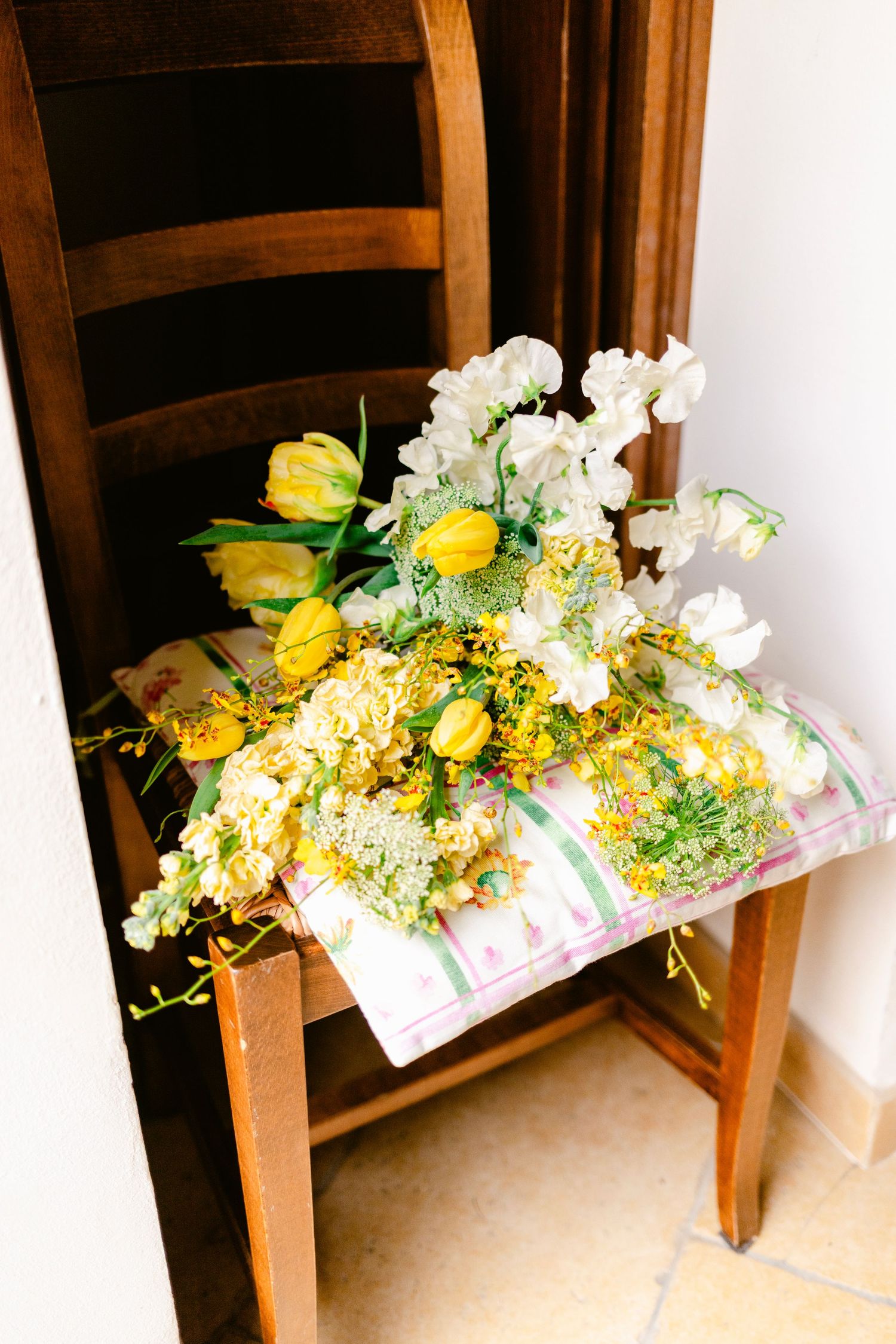 Elegant floral arrangements with yellow and white flowers displayed on wooden chairs.