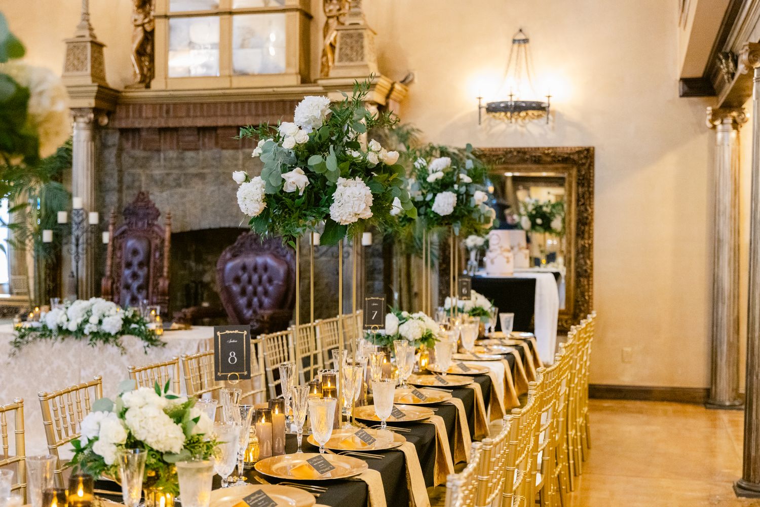 Elegant wedding reception hall with long tables decorated in gold and white, featuring floral centerpieces and crystal chandeliers.