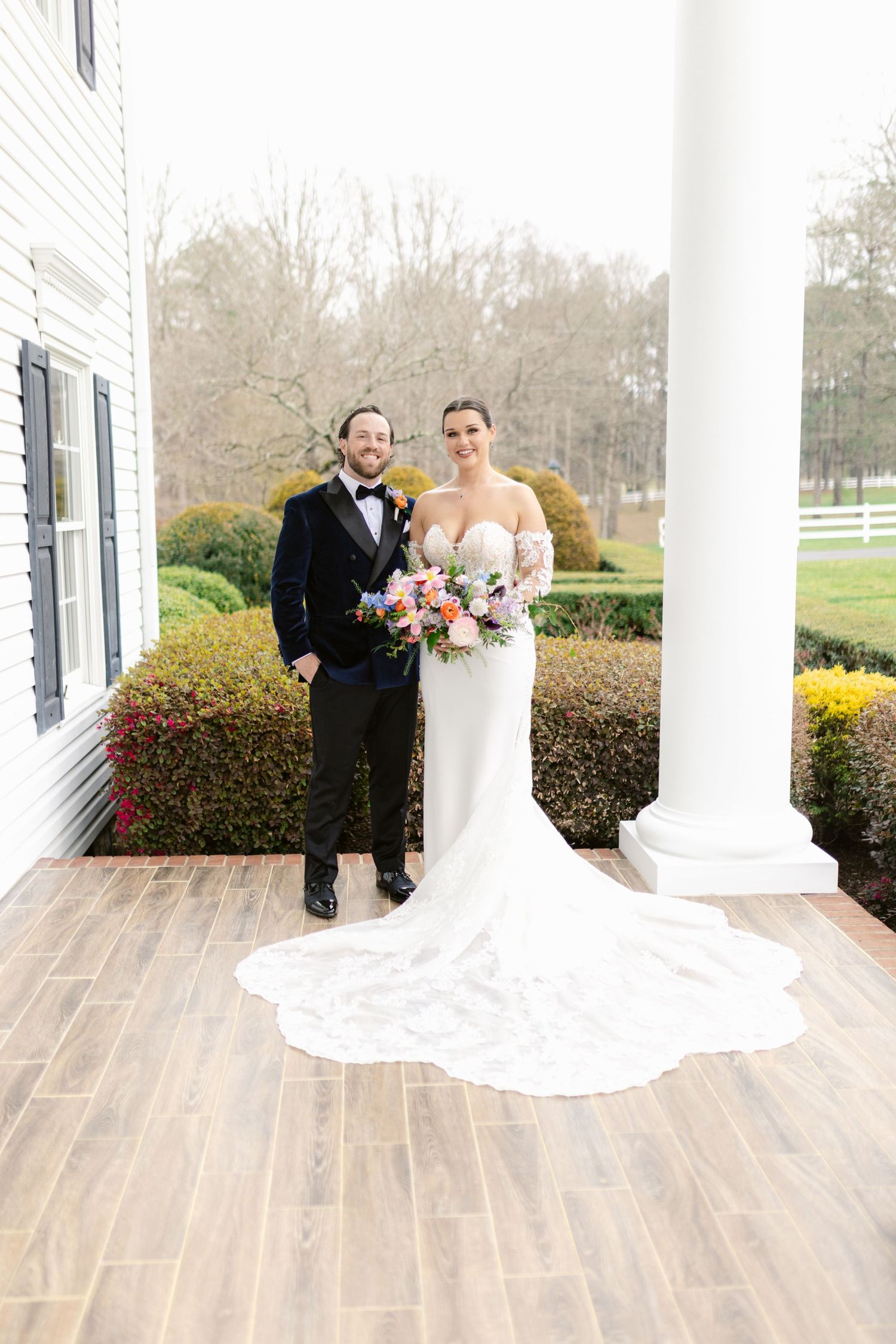 Wedding portrait on historic mansion porch with white columns and wooden flooring.