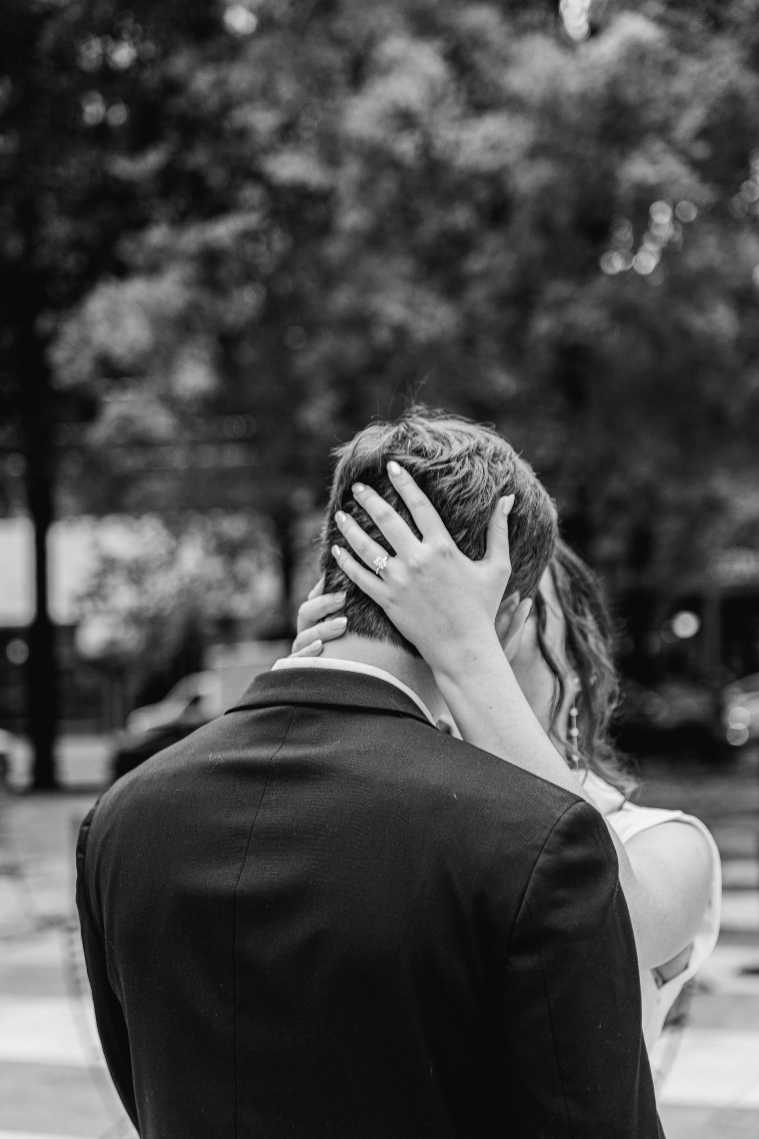 Black and white photo showing a tender romantic moment as a woman's hand rests on her partners head outdoors.