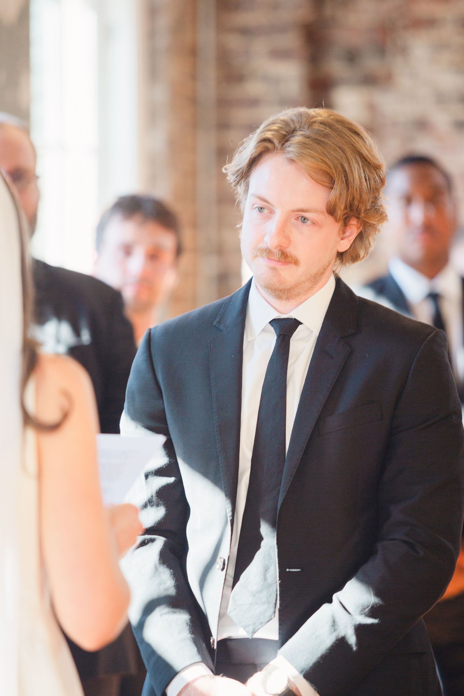 Wedding ceremony inside a rustic brick venue showing formal attire and traditional decor.