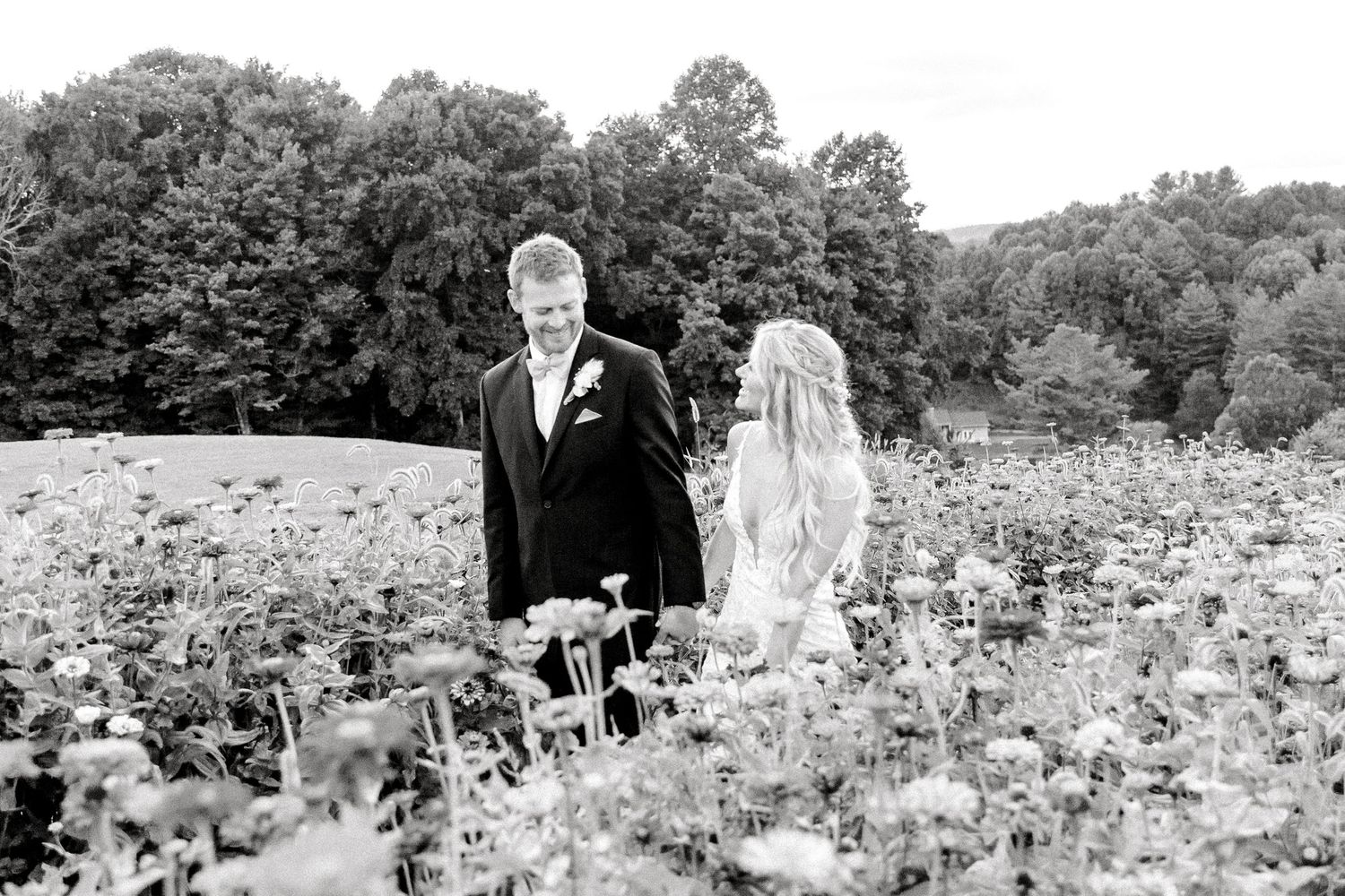 Black and white wedding photo of couple standing in wildflower meadow.