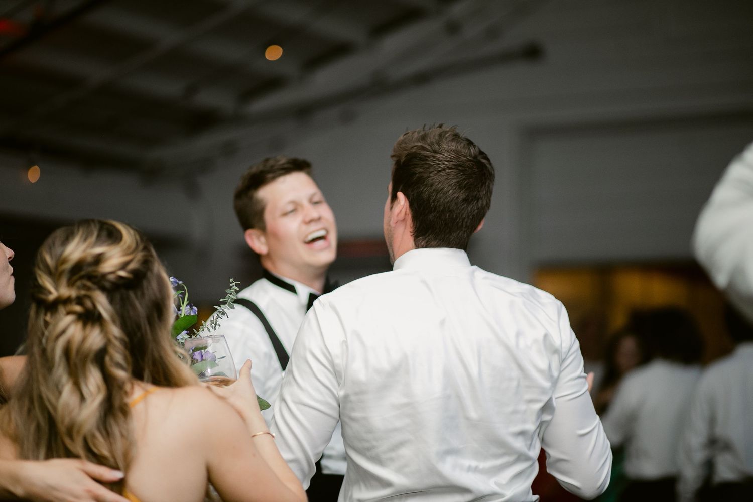 Wedding guests dancing and laughing during reception celebration.