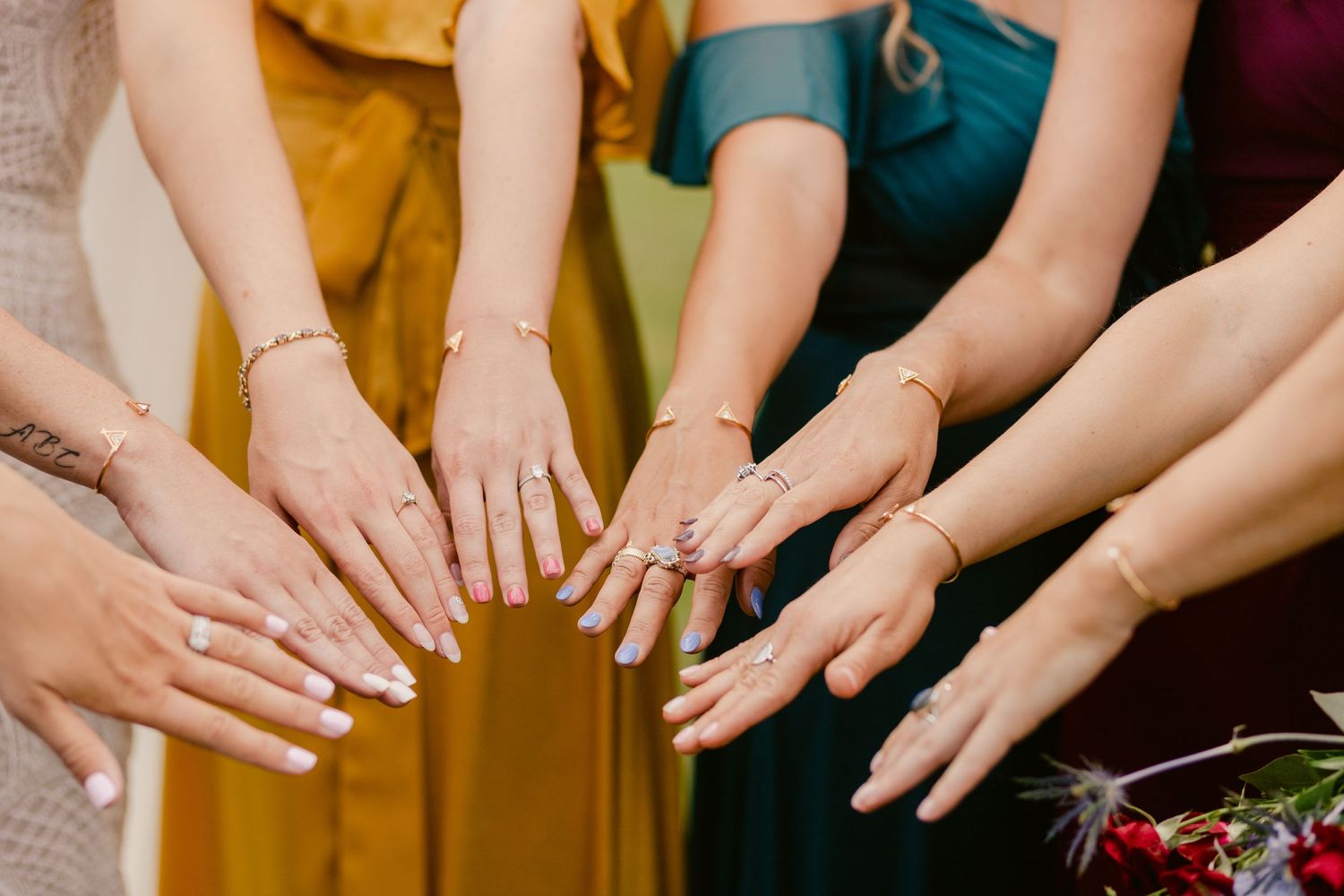 A group of hands displaying rings and manicured nails in colorful formal dresses at a special event.