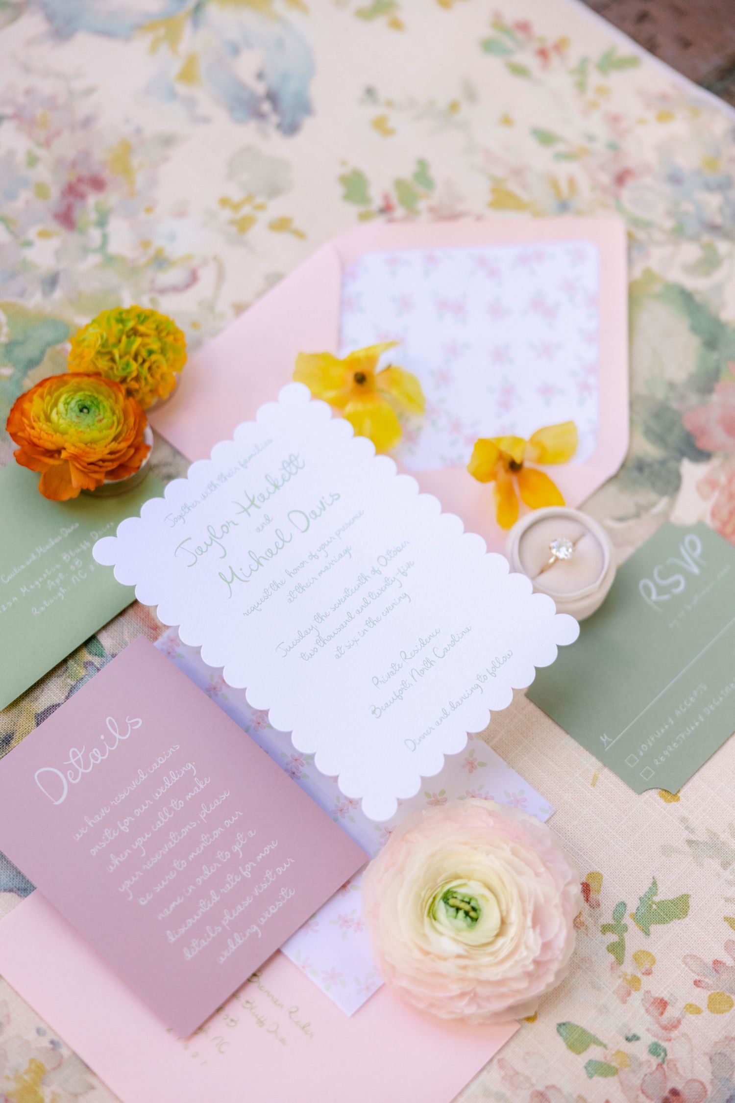 Wedding invitation suite with pink and white scalloped cards decorated with orange ranunculus flowers on a floral background.
