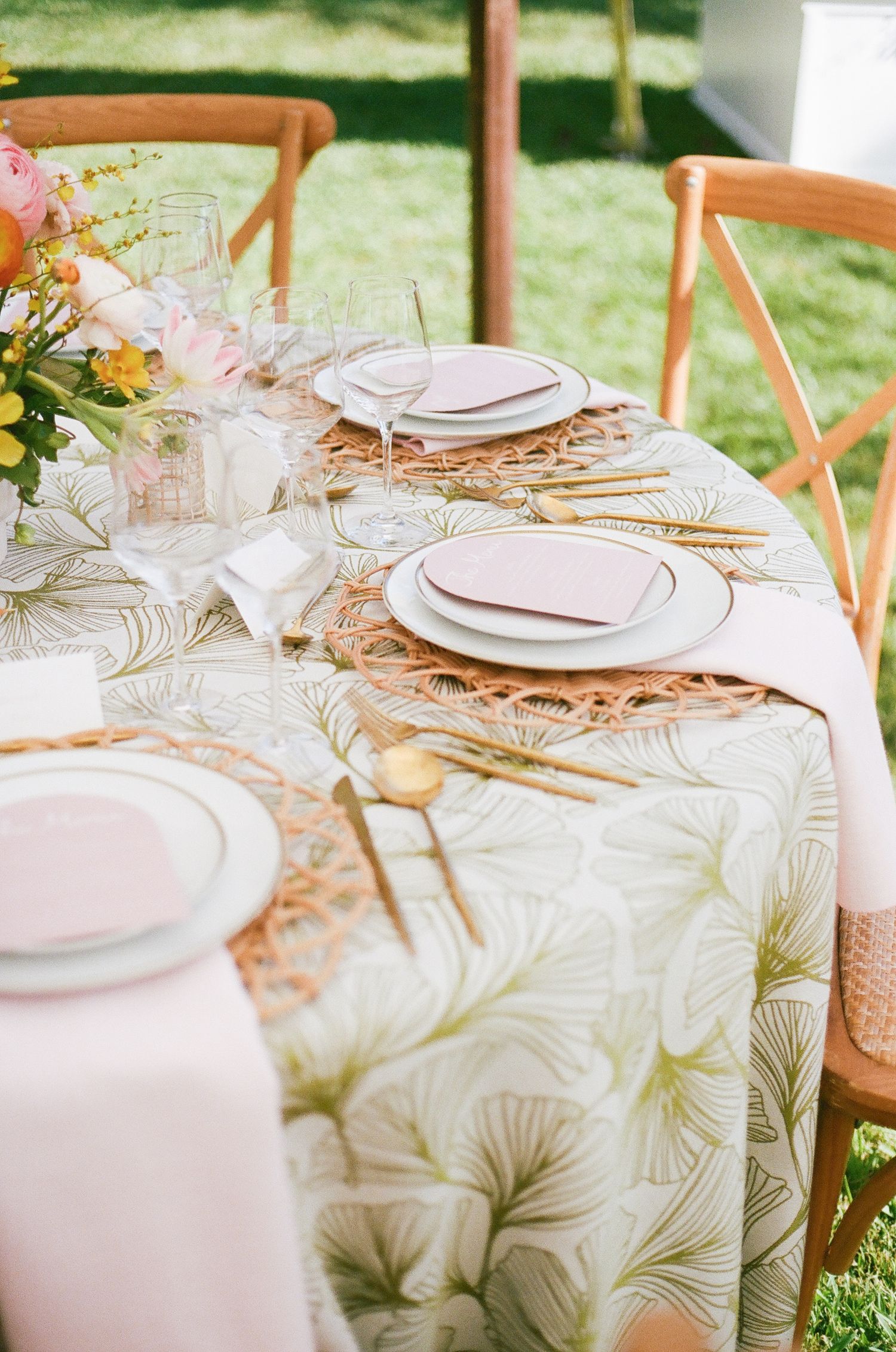 Elegant table settings with rose gold charger plates and delicate floral tablecloths at an outdoor wedding reception.