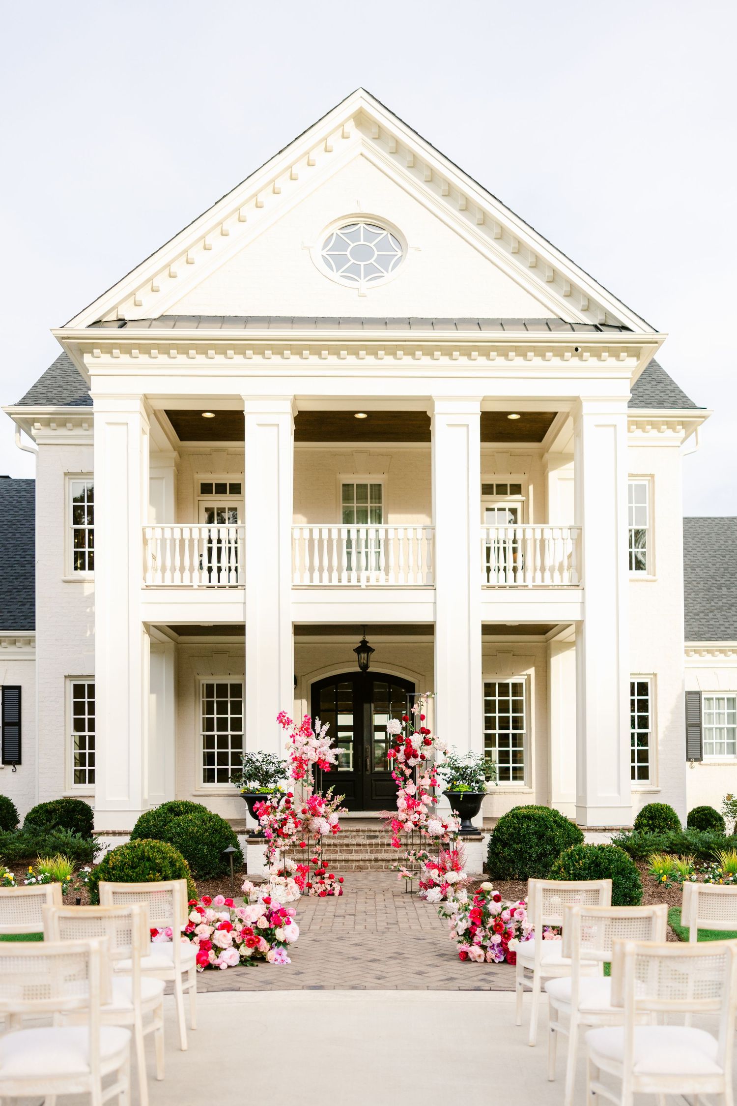 Grand white mansion wedding venue with columns and pink floral accents along the entrance.