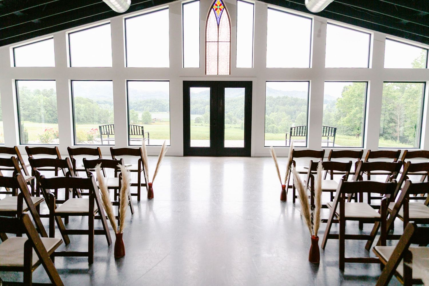 Modern dining hall interior with long wooden tables and chairs arranged in rows near large windows with natural lighting.