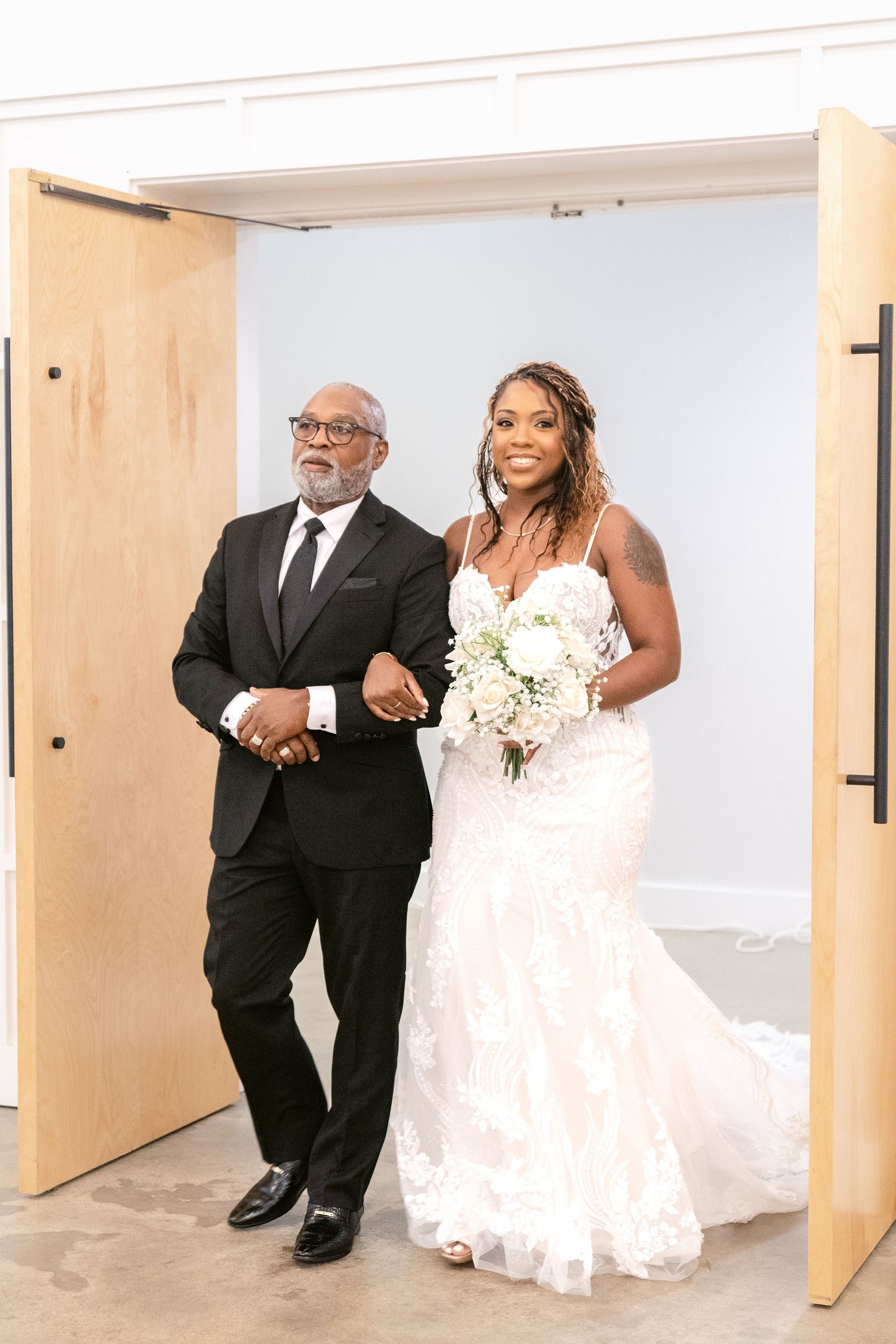 A bride in a white wedding dress walks down a hallway with her escort before the ceremony.