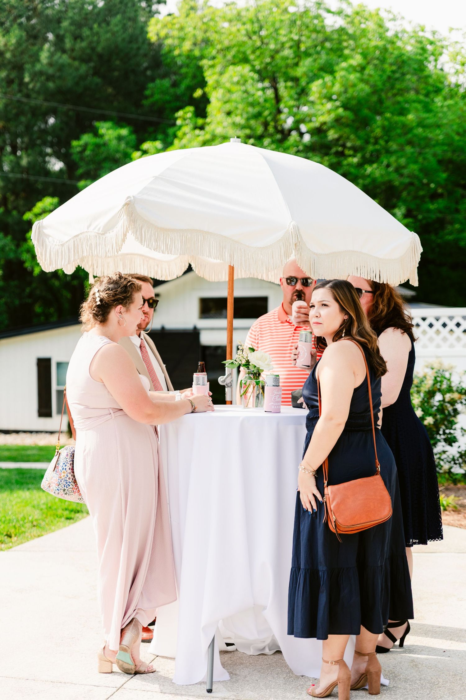 Party guests gather under white parasols at outdoor cocktail tables during a summer event.