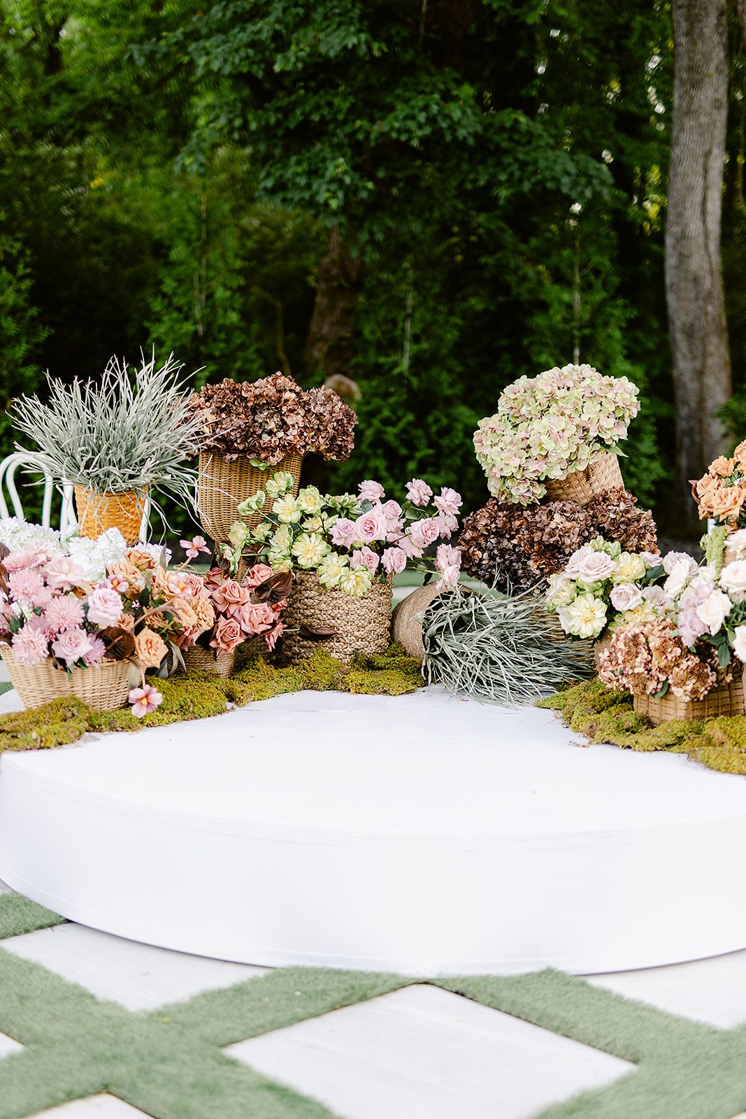 Elegant floral arrangements with pink and white blooms line a curved white wall at an outdoor garden wedding venue.