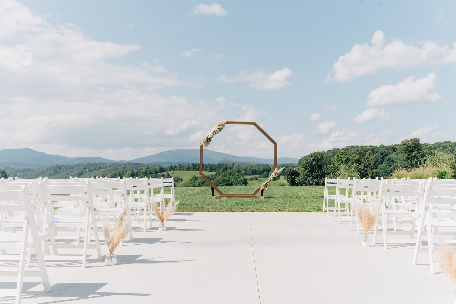 White folding chairs arranged in rows for an outdoor wedding ceremony with mountains and blue sky in the background.