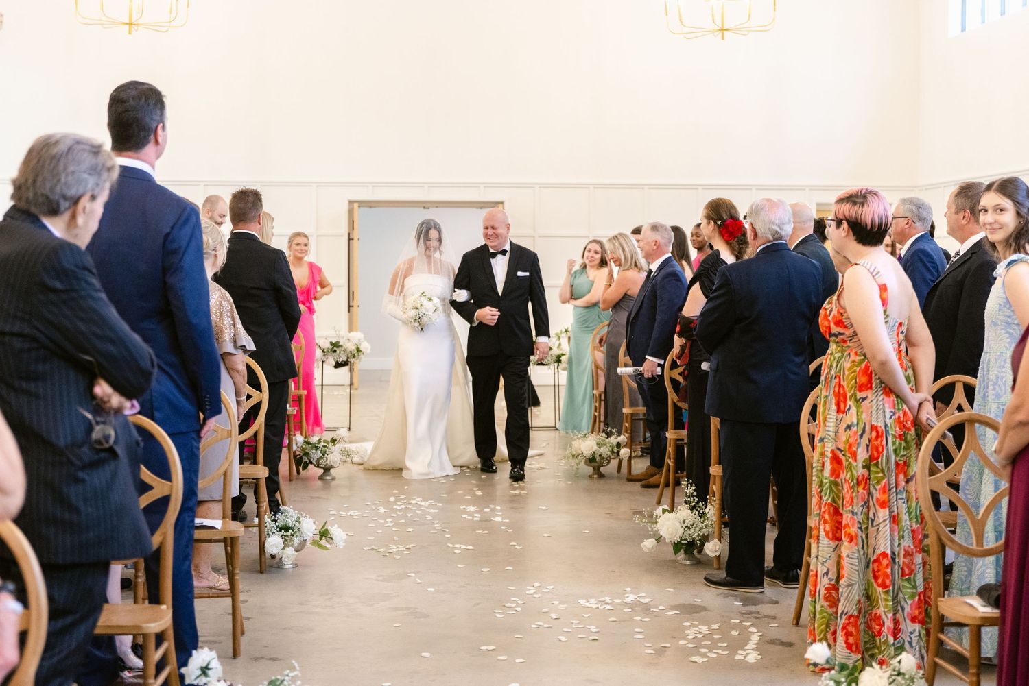 A panoramic view of wedding guests seated in rows at an elegant indoor ceremony venue with white decor.