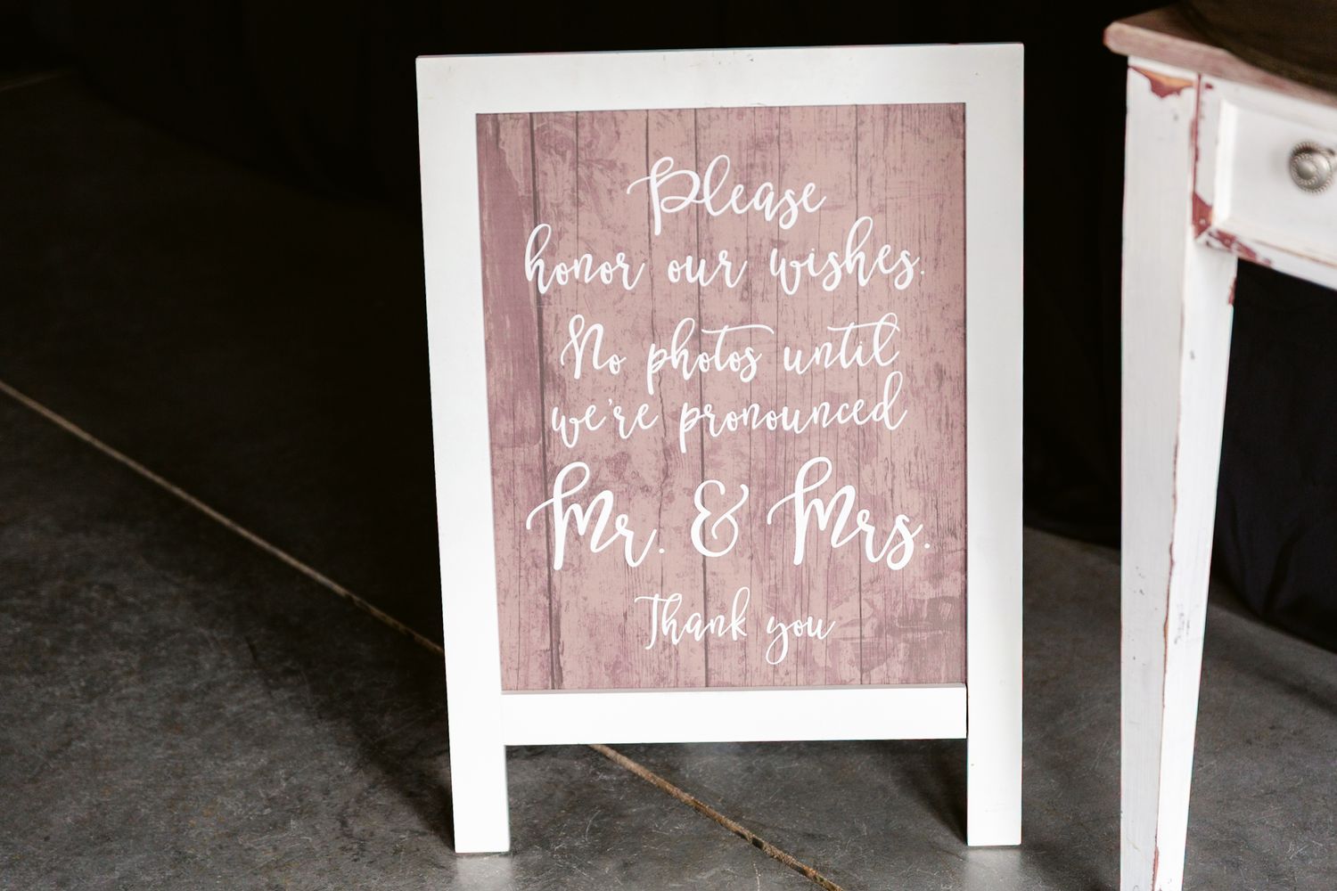 Wedding reception signs with rustic pink text on wooden boards display romantic messages and seating directions.