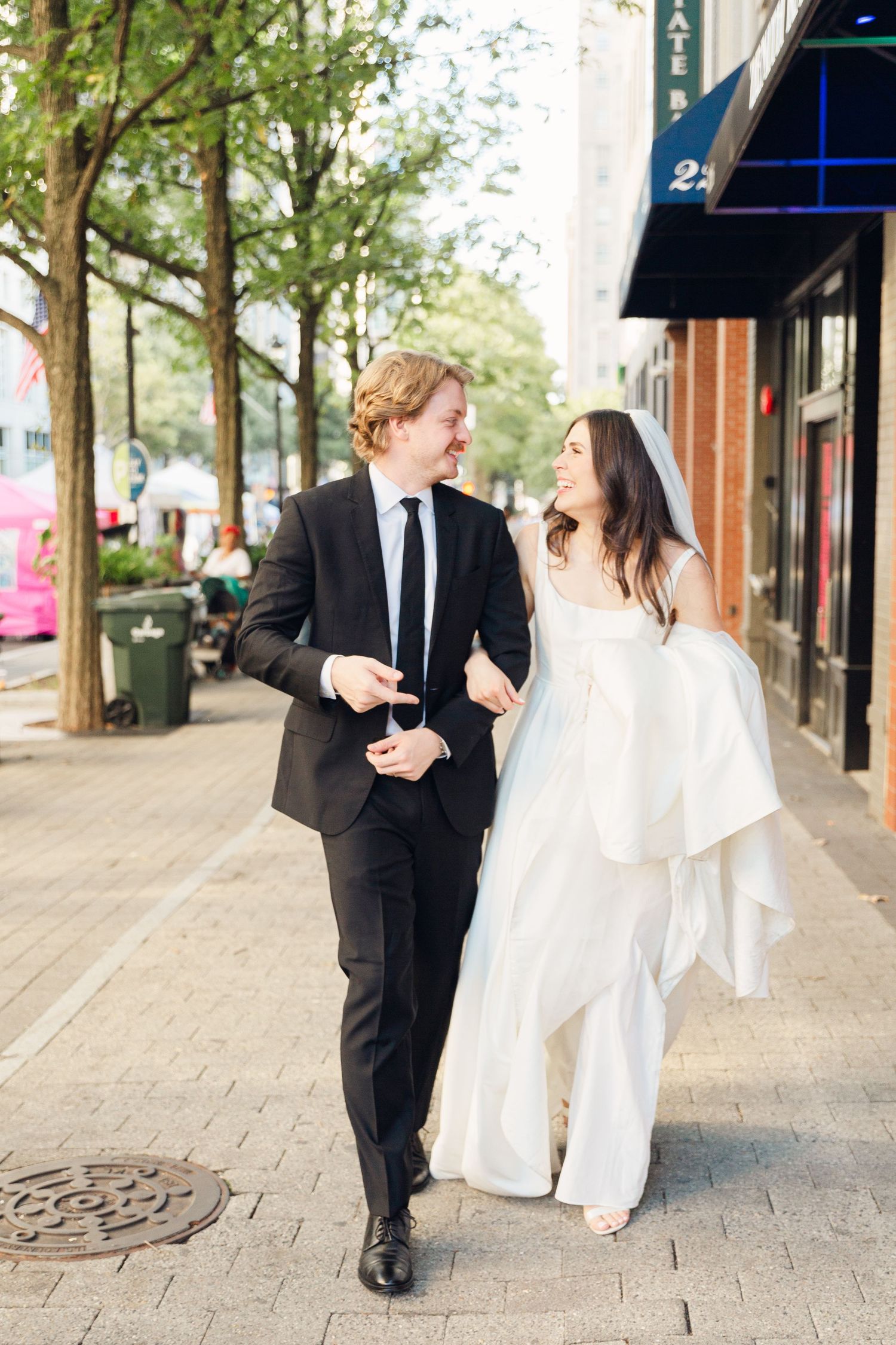 Couple walking and laughing together on brick sidewalk during wedding photoshoot.