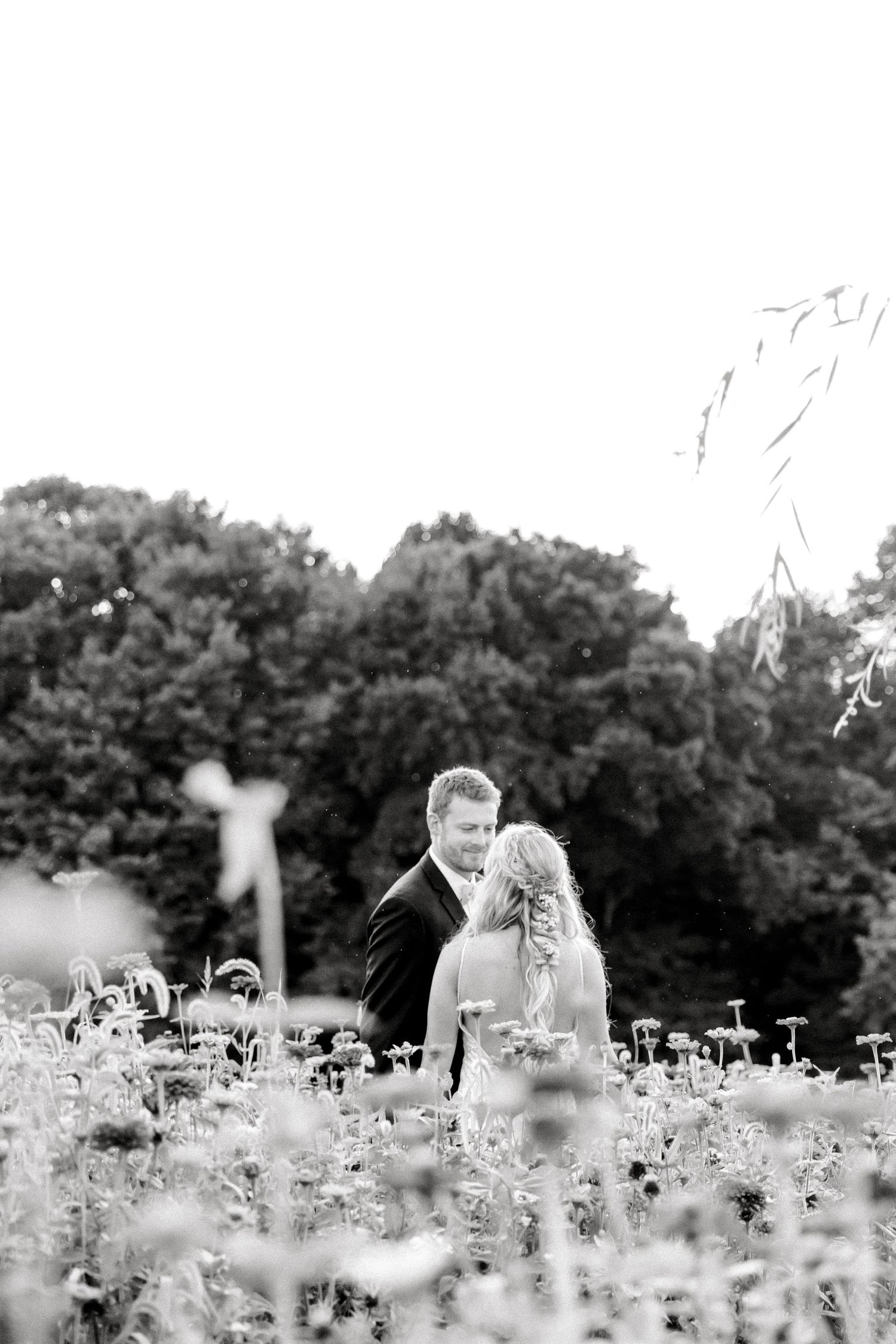 Black and white portrait of newlyweds among wildflowers in a meadow.