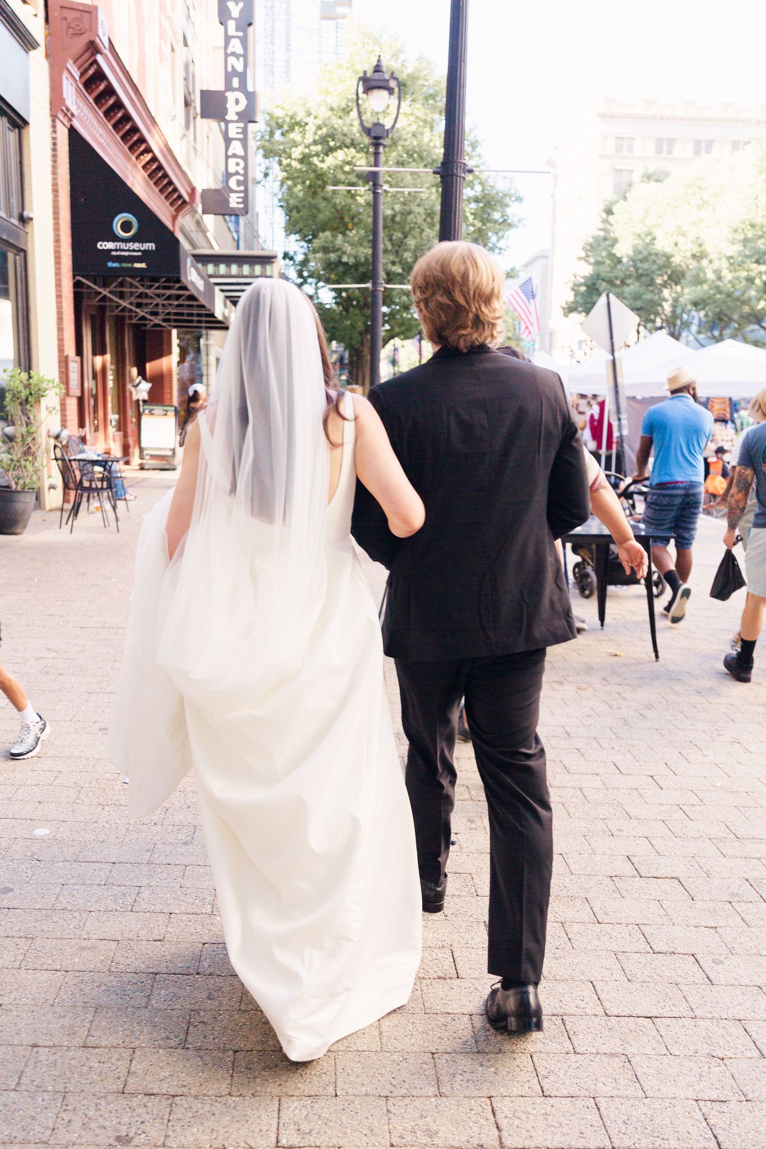 A couple walking down a city sidewalk, with the bride in a flowing white dress and veil.