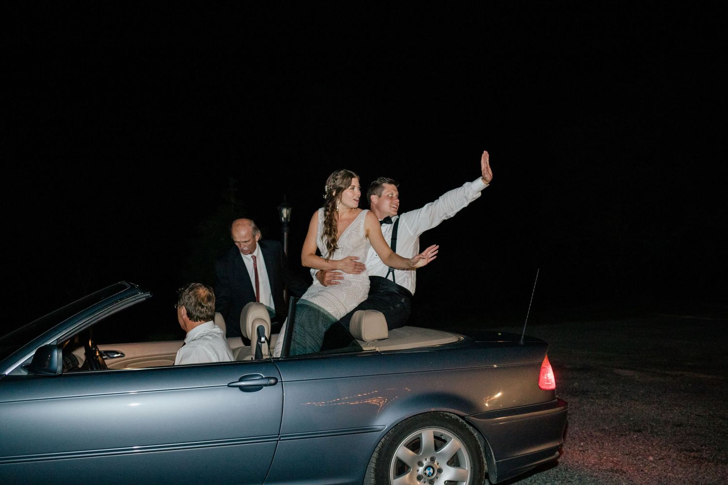 Wedding party poses dramatically in convertible car at night.
