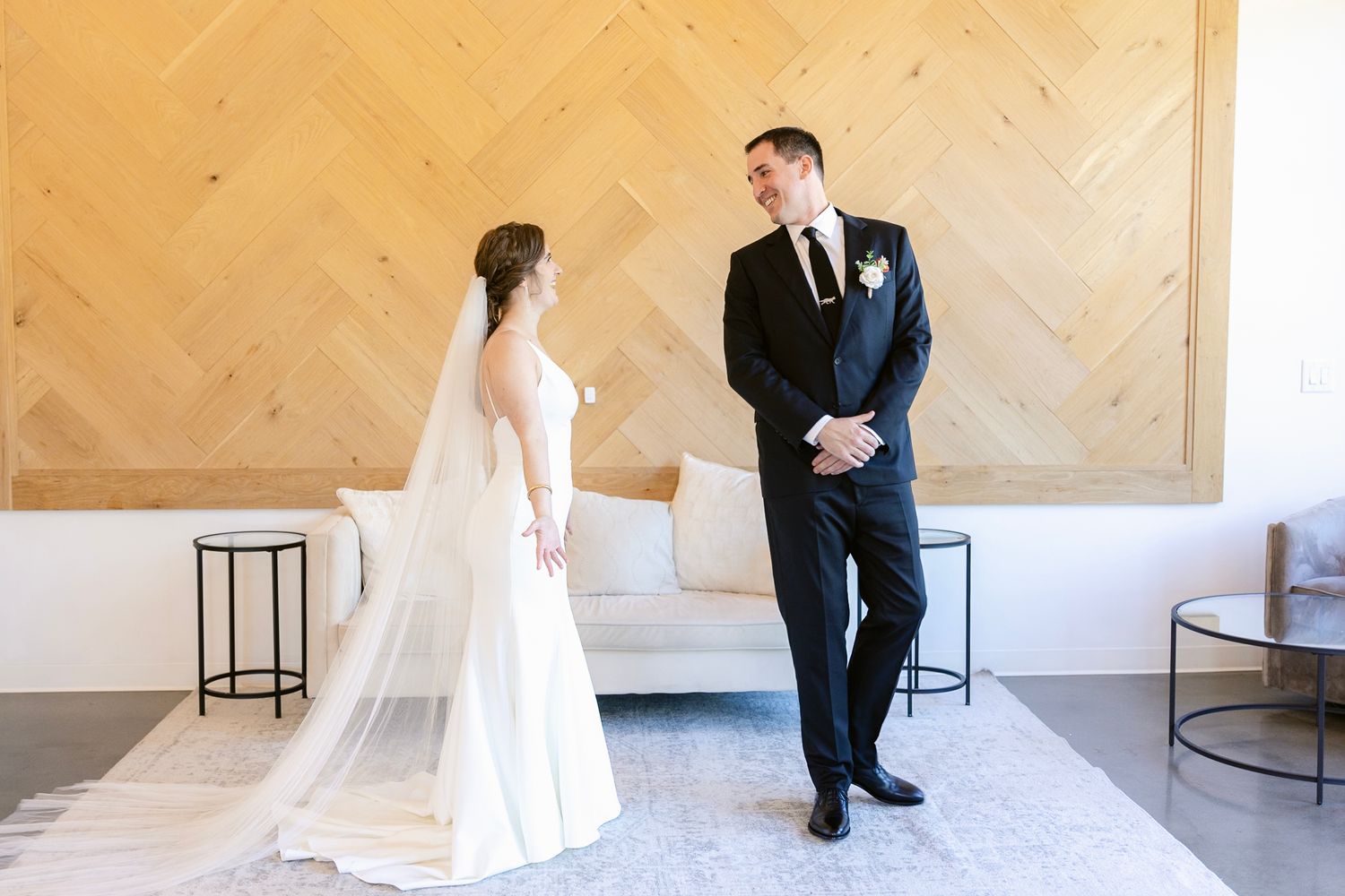 A first look moment between a couple in wedding attire standing in an elegant room with geometric wall details.