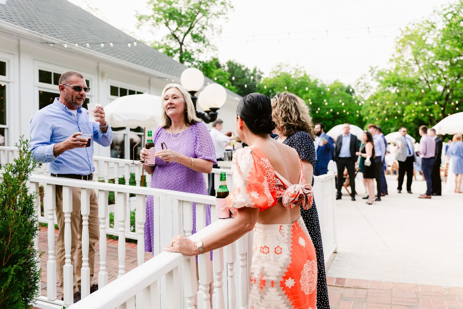 Wedding guests mingle and socialize on an elegant white porch during an outdoor reception celebration.