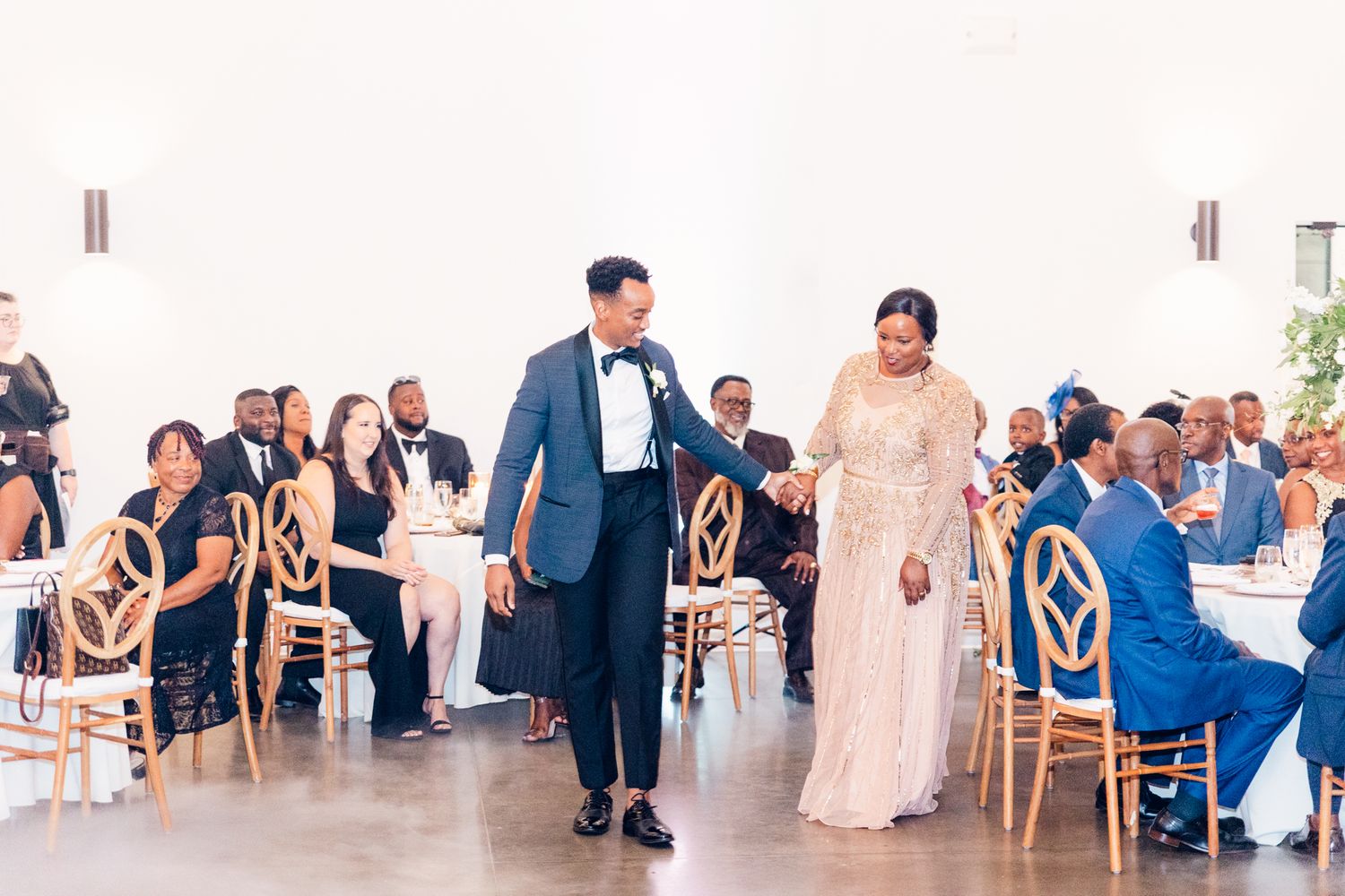 Wedding guests seated at elegant round tables with gold chairs during a reception celebration.