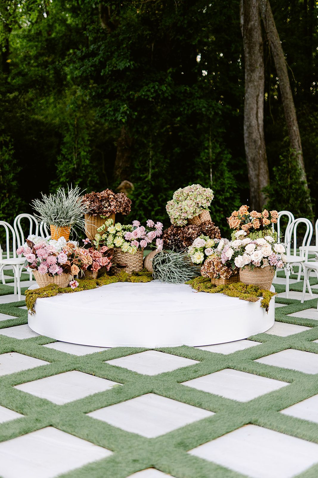 Outdoor wedding ceremony setup with white chairs and floral arrangements along a geometric patterned walkway.