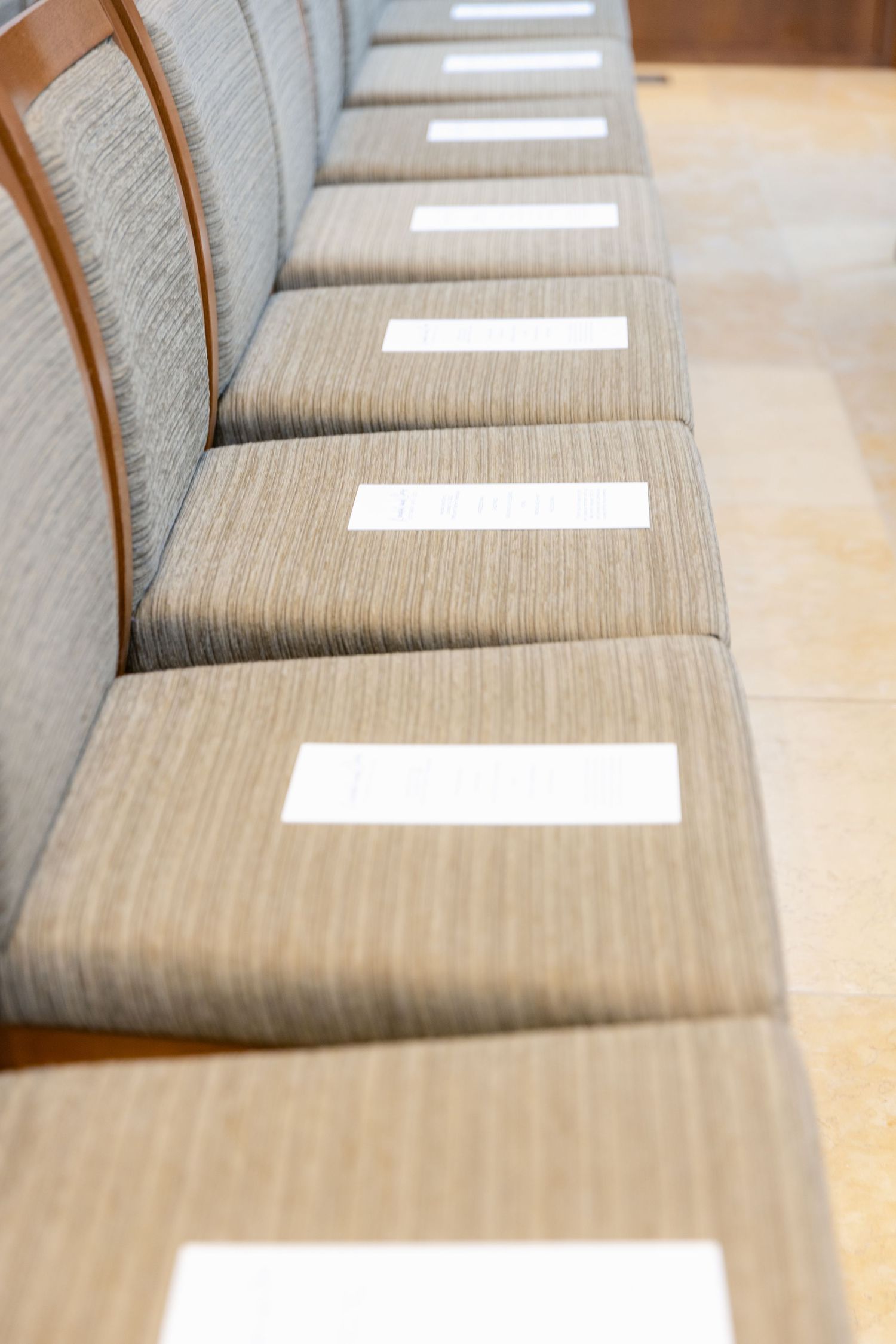 Row of gray upholstered chairs with white programs placed on seats for a wedding ceremony.