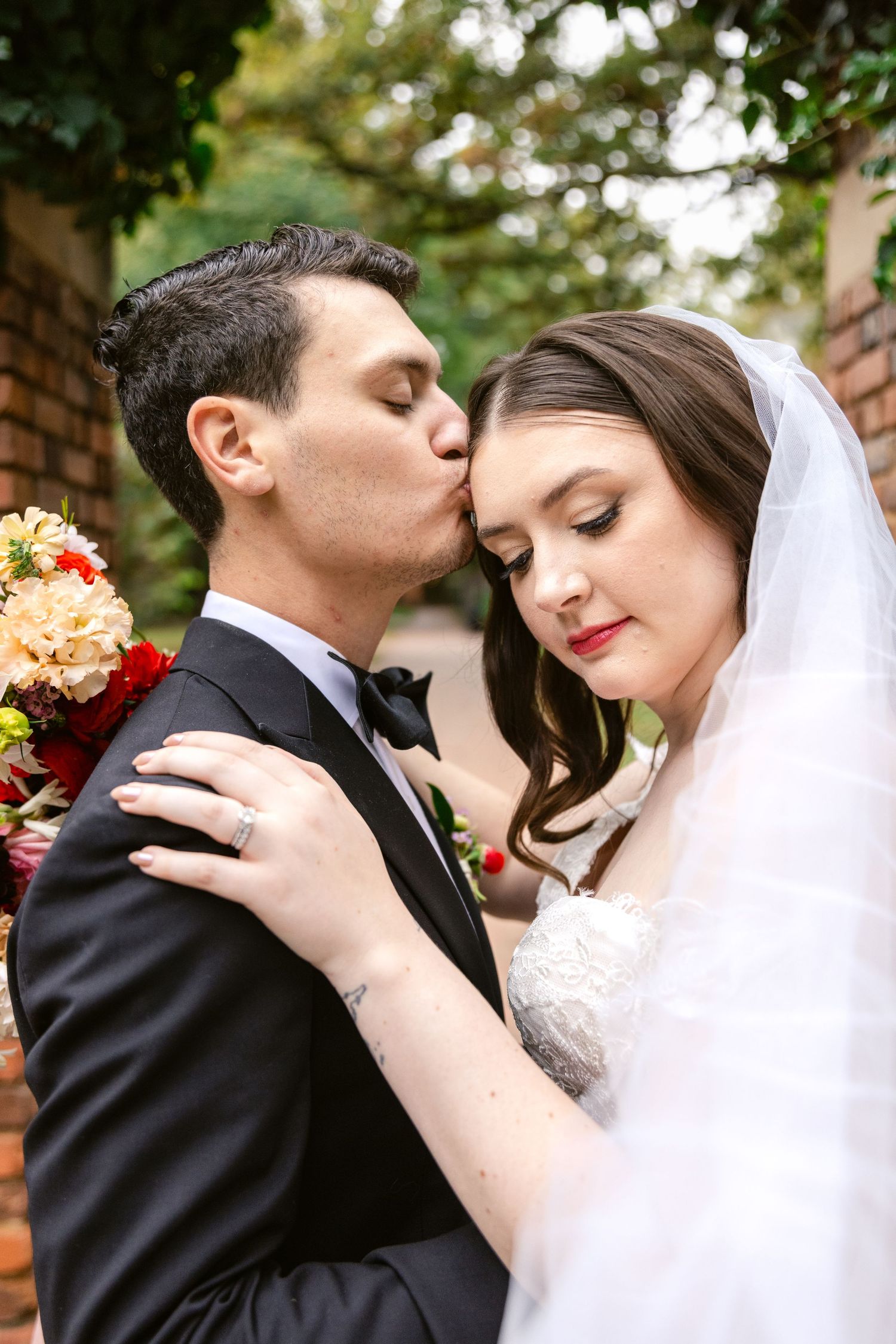 A romantic wedding couple embracing in an outdoor garden setting with lush greenery in the background.