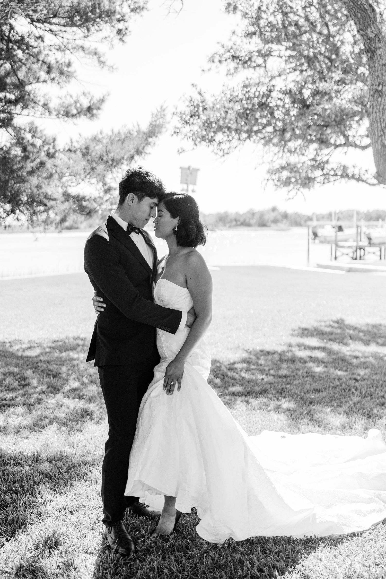 A romantic black and white wedding photo capturing a tender moment between newlyweds outdoors.