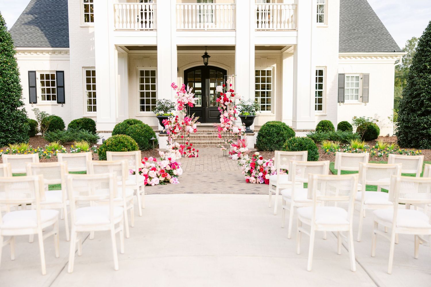 Elegant white mansion wedding venue with pink floral aisle decorations and white chairs set up for outdoor ceremony.