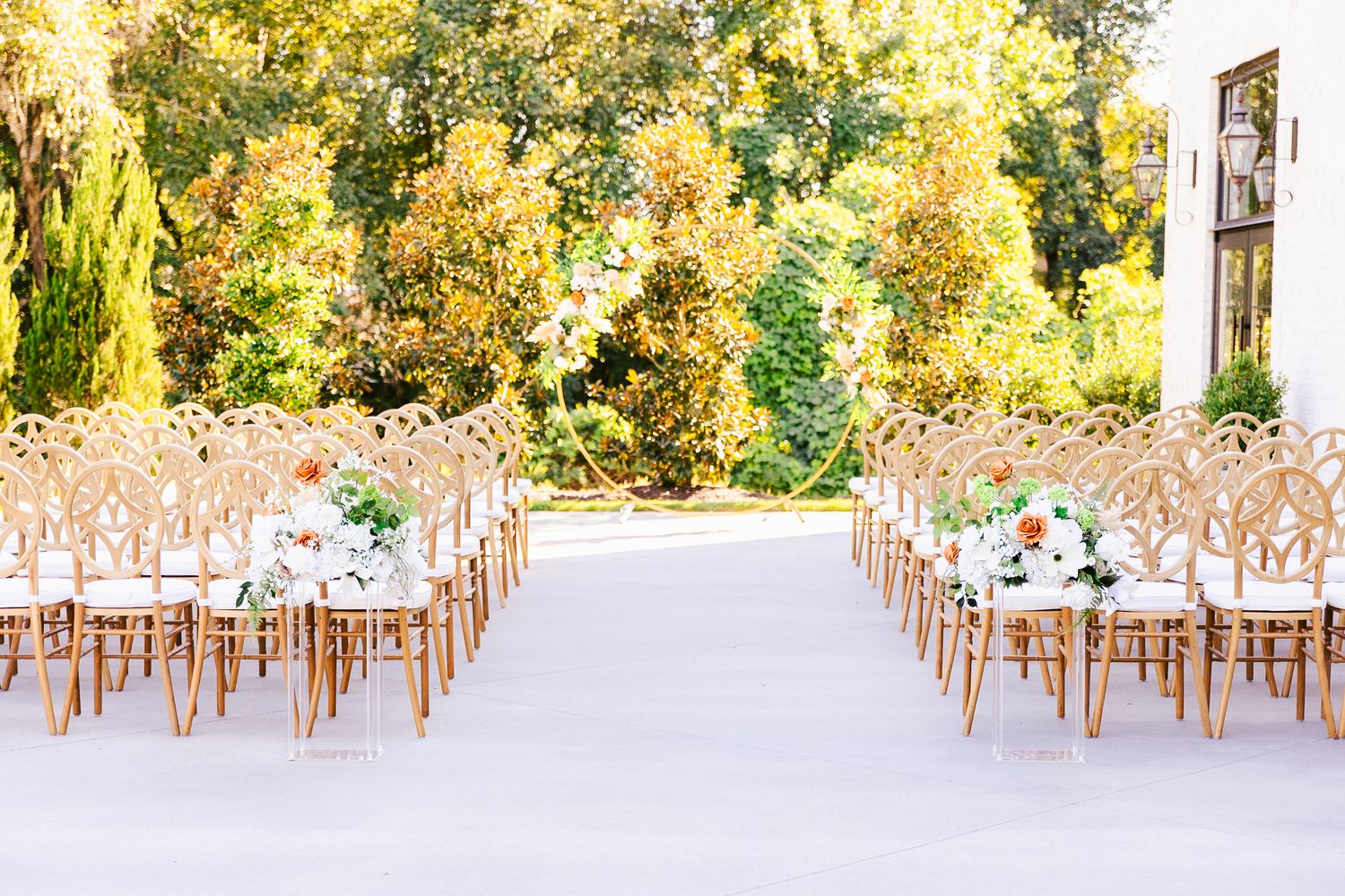 Panoramic view of an elegant outdoor wedding venue with wooden chairs arranged in rows under golden sunlight.