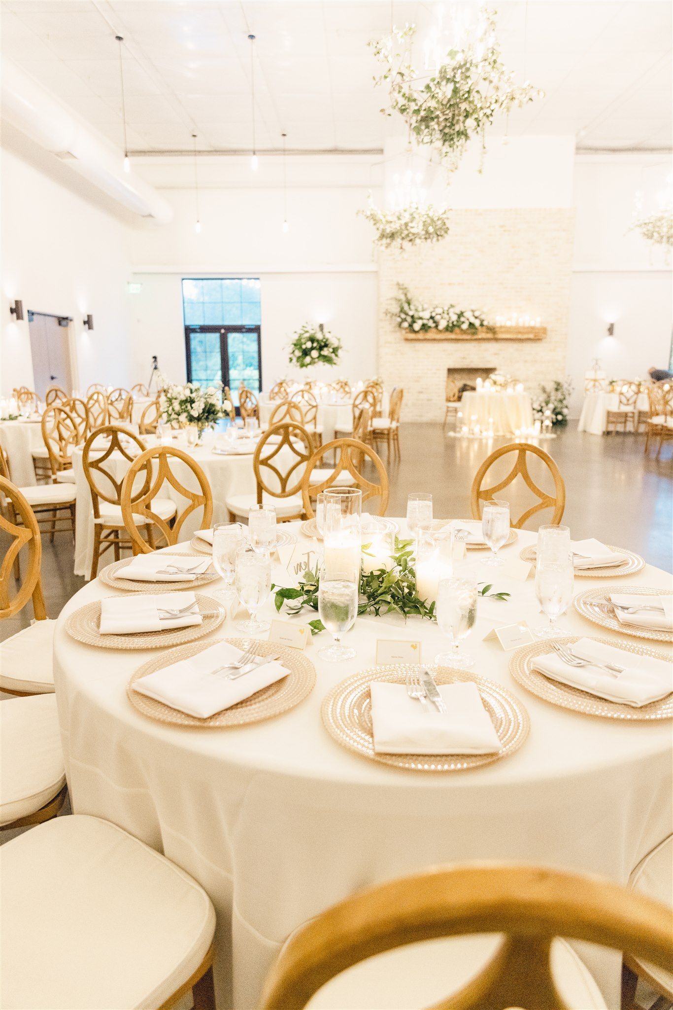 Elegant wedding reception tables set with white linens, gold chairs, and delicate floral centerpieces in a bright venue.