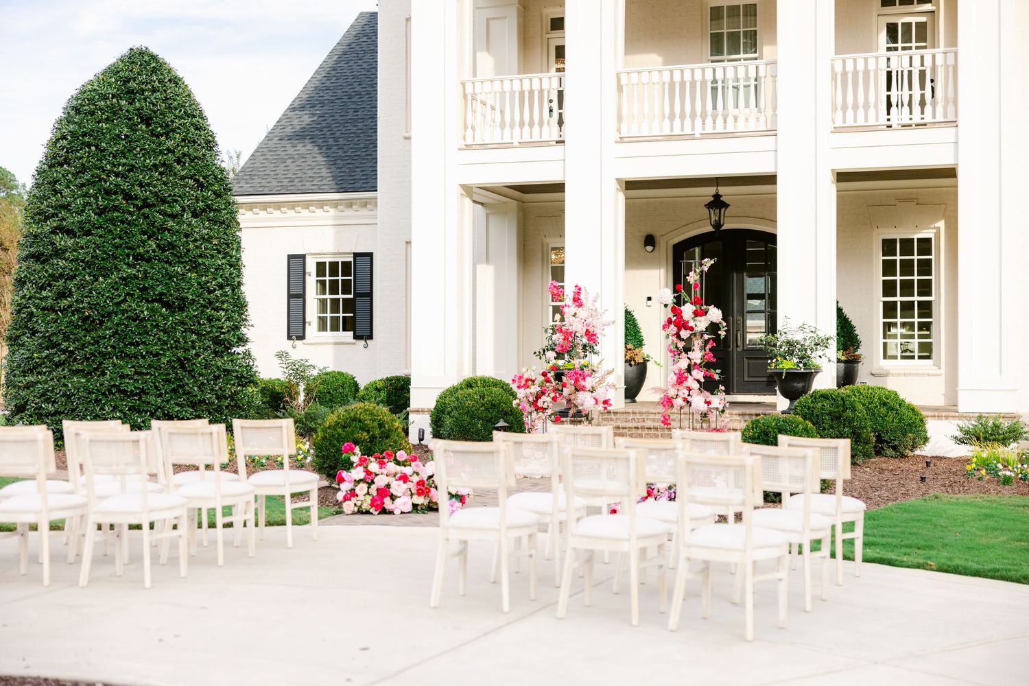 Classic white colonial-style wedding venue exterior with pink floral decorations and white chairs.