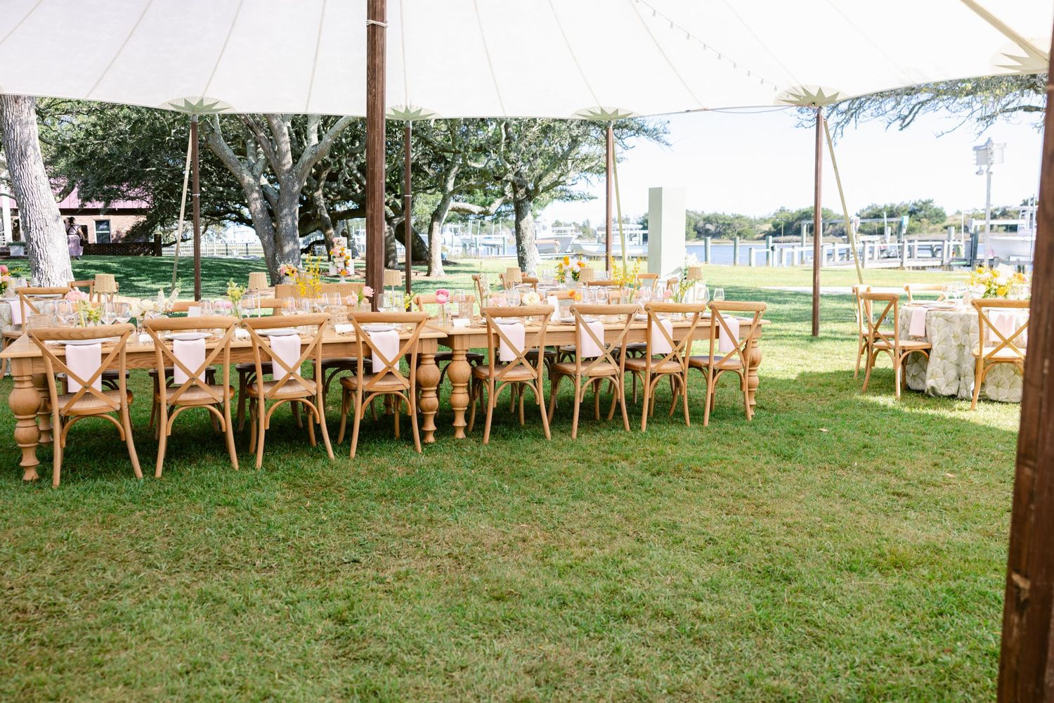 White wedding tents and wooden chairs arranged on a lush green lawn for an outdoor celebration.