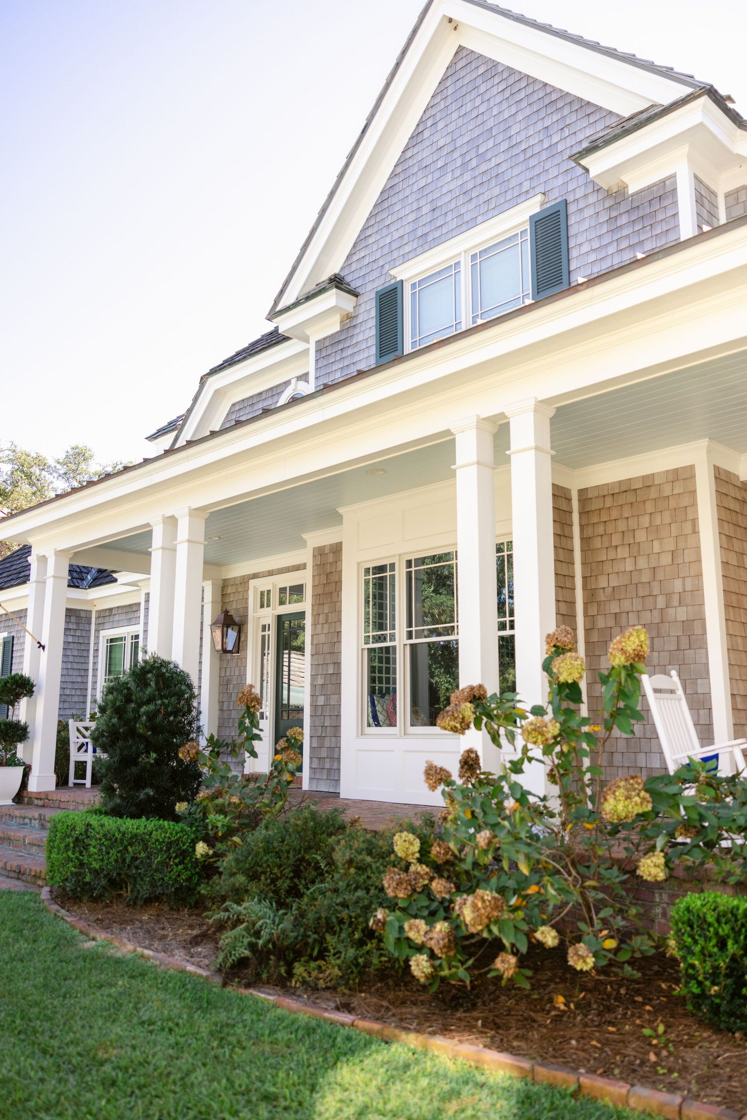 Exterior view of a craftsman style home with white trim and landscaped garden beds featuring yellow blooming flowers.