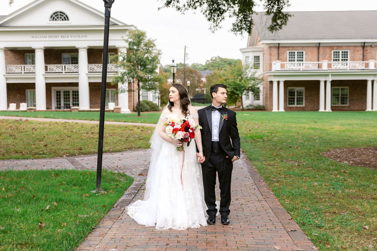 A couple walking together on a brick pathway between white colonial-style buildings.