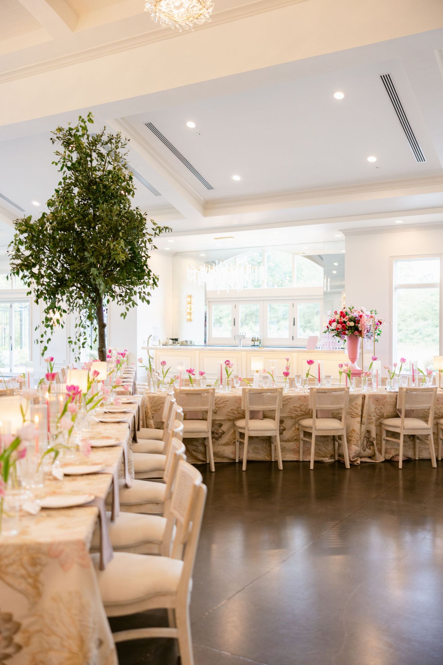 Elegant wedding reception venue with cream chair covers, tall centerpieces, and recessed lighting in a modern ballroom setting.