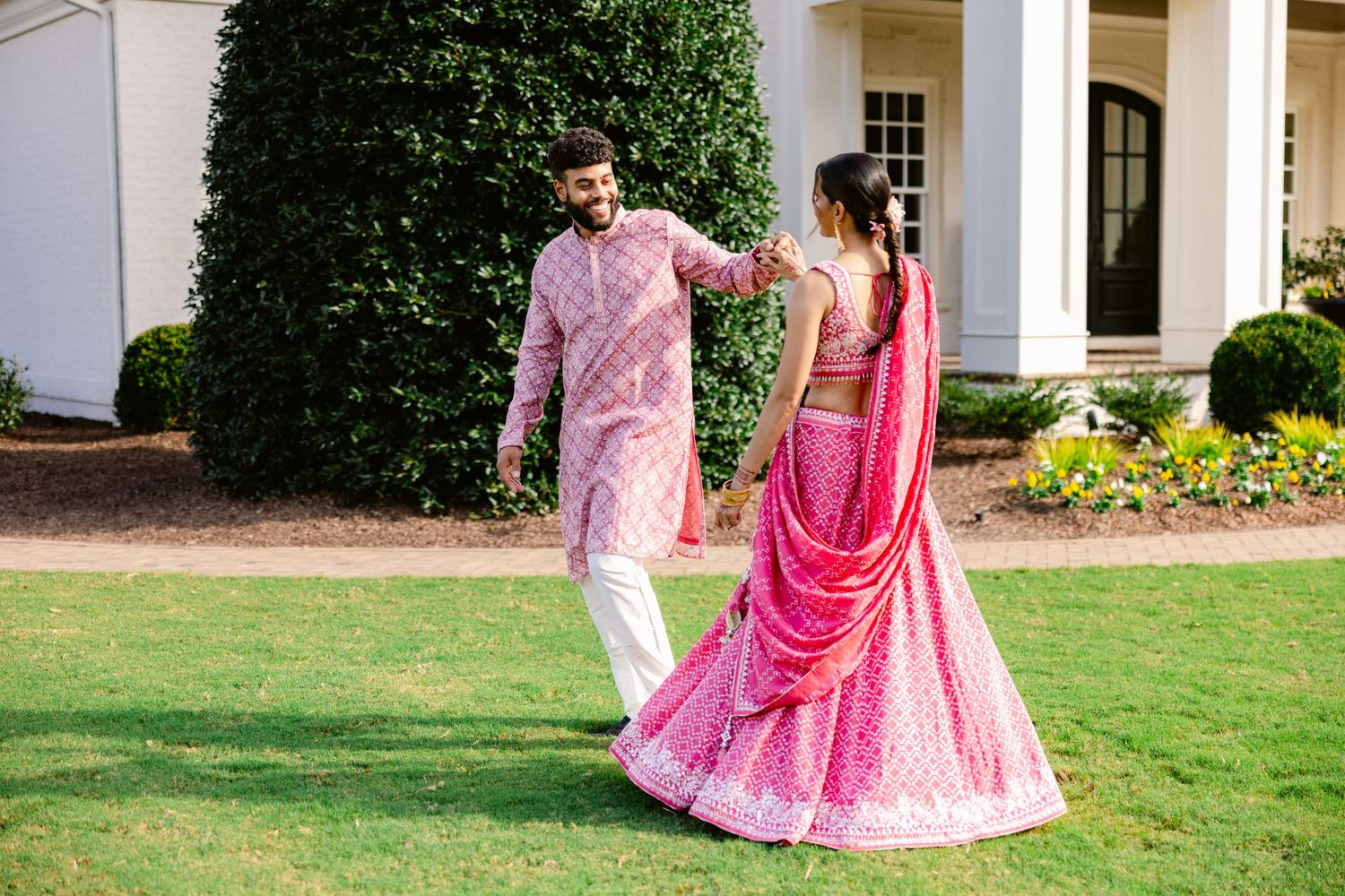A couple in traditional Indian wedding attire walking through a garden setting.