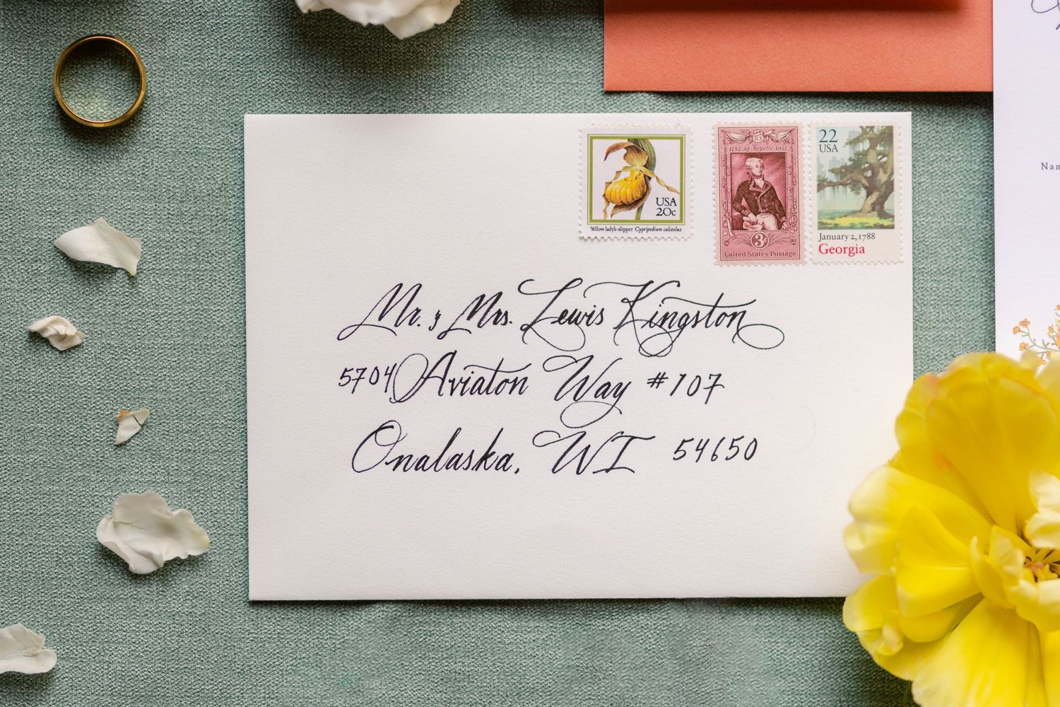 Wedding stationery and invitation details laid out on sage green background with yellow daffodils and white petals.